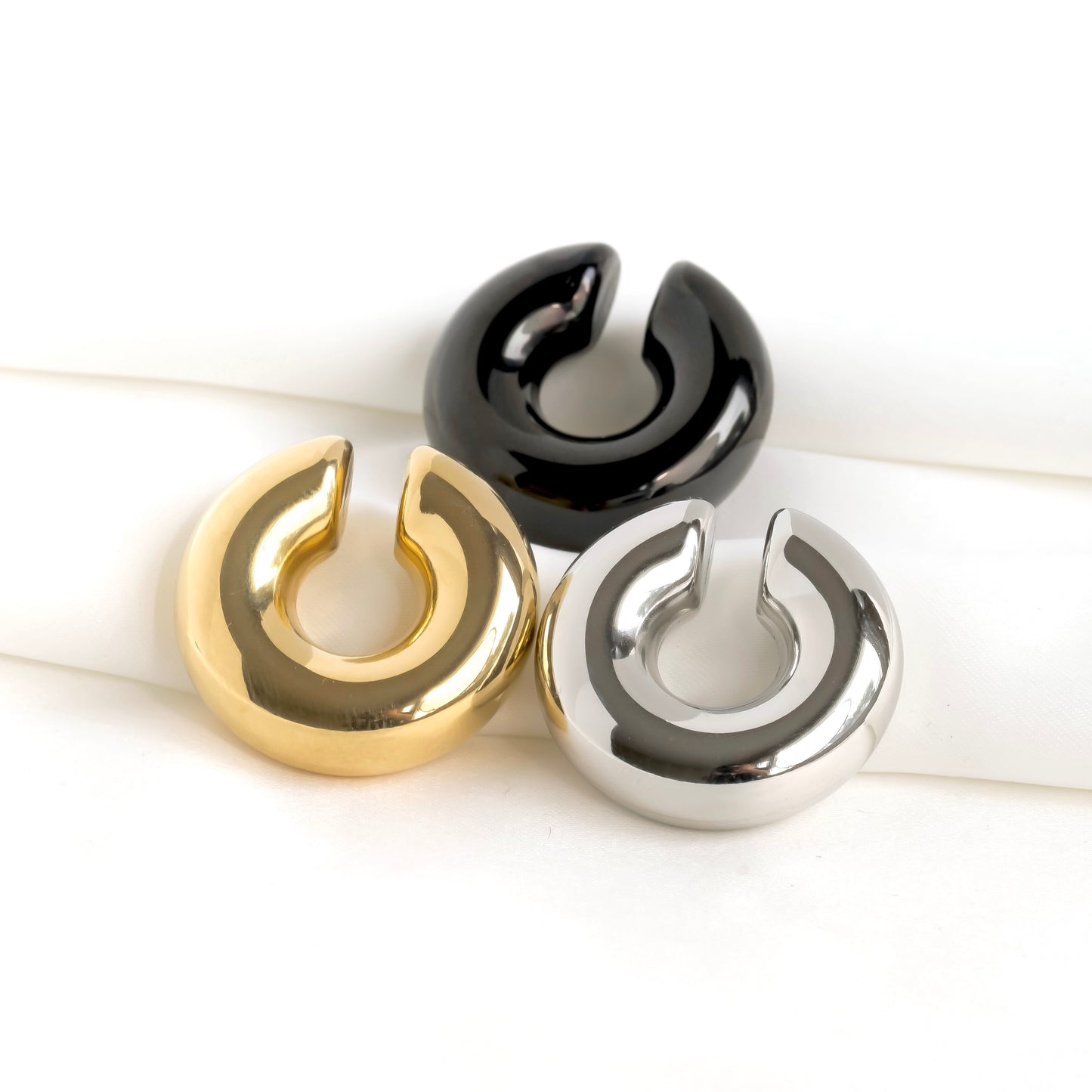 Three metallic bold ear cuffs in gold, black, and silver on a white background
