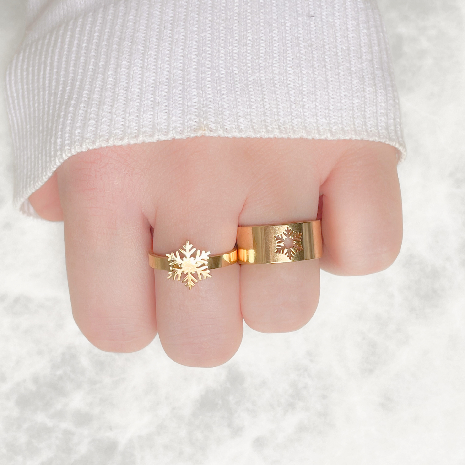 Top view of two gold rings with snowflake design worn on a finger against a white background