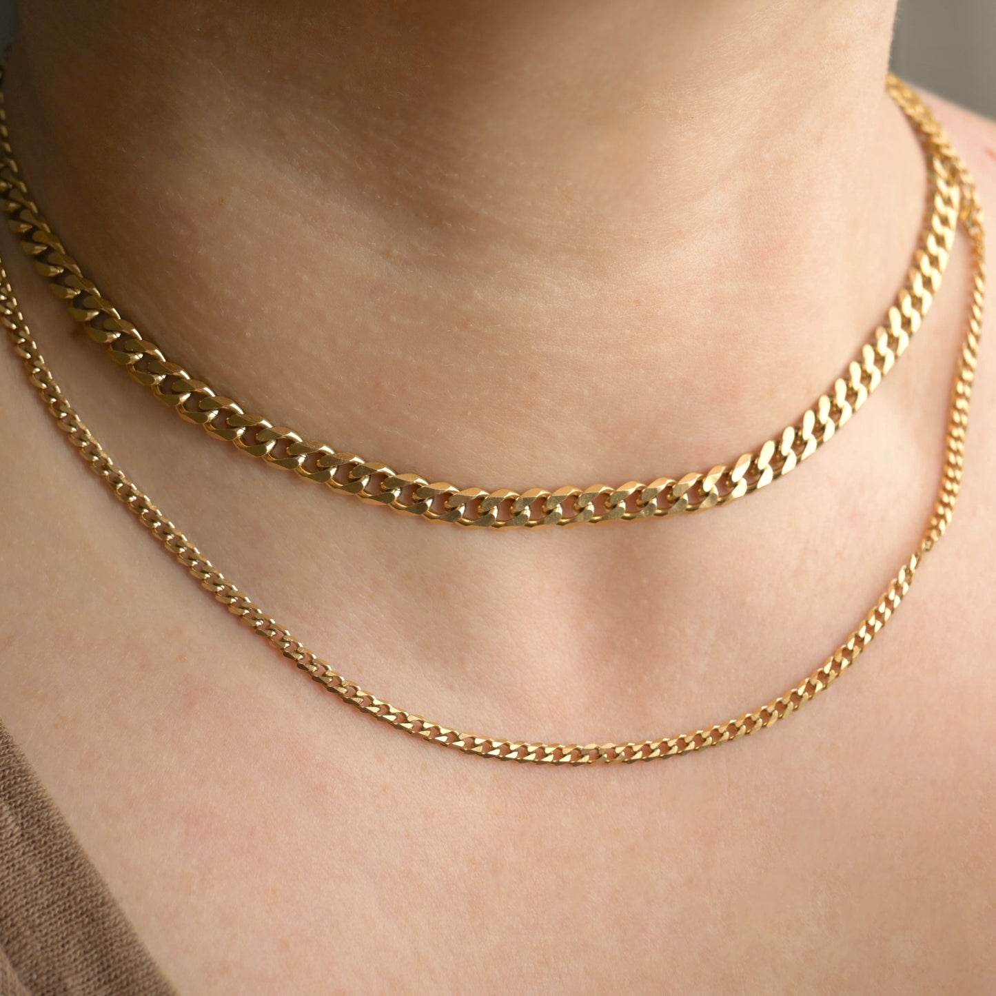 Front view of two gold cuban link necklaces, one thick and one thin, on a person's neck