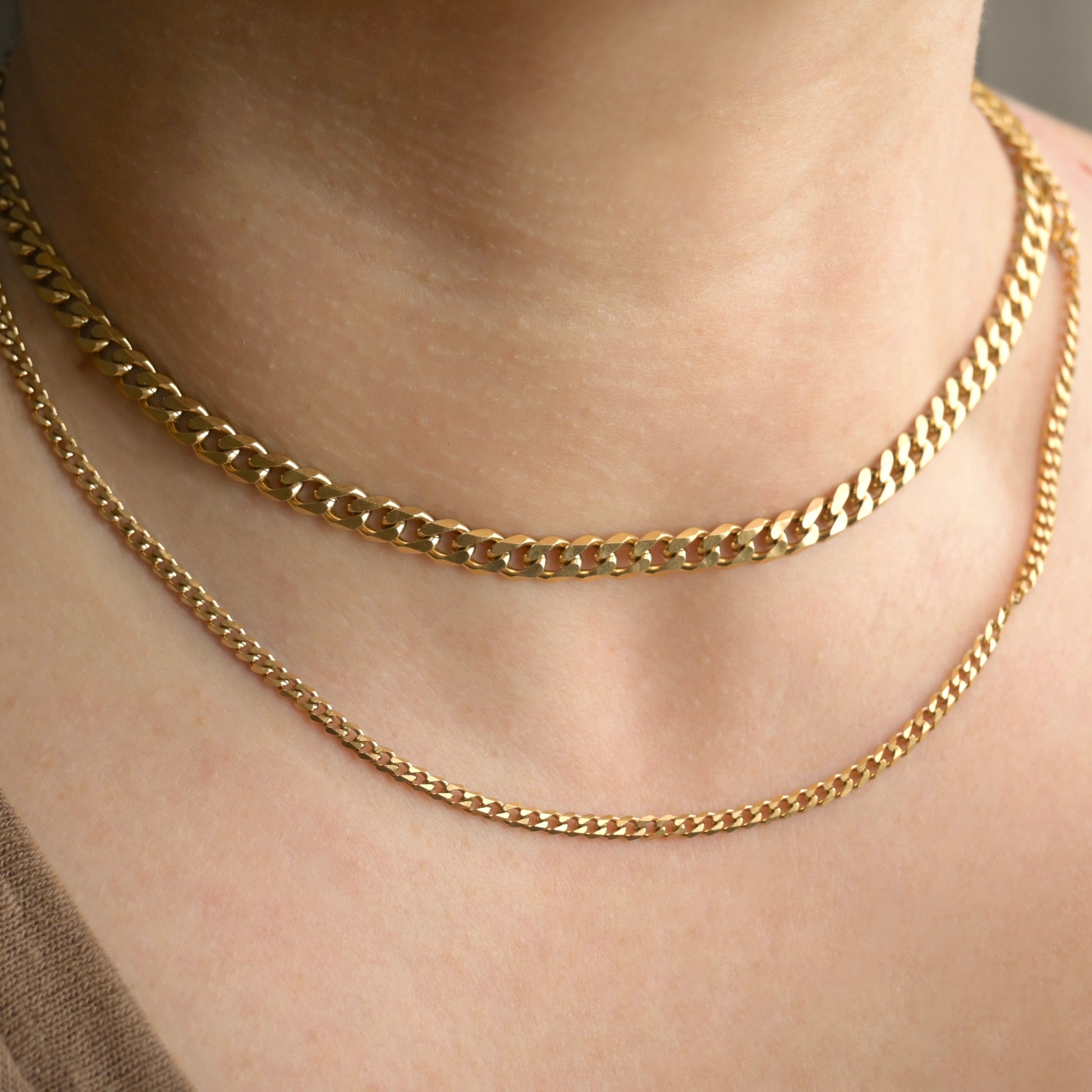 Front view of two gold cuban link necklaces, one thick and one thin, on a person's neck