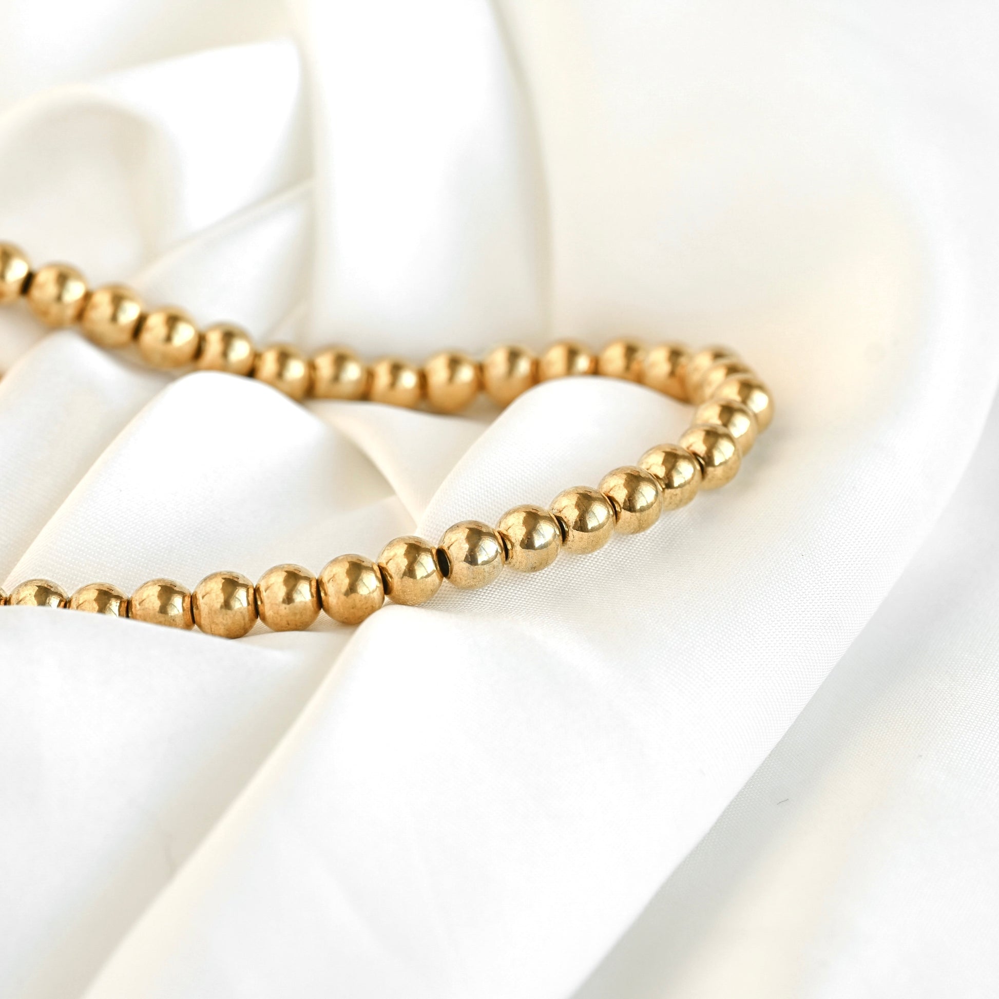 A strand of small, polished gold-colored beads draped elegantly over soft, white satin fabric.