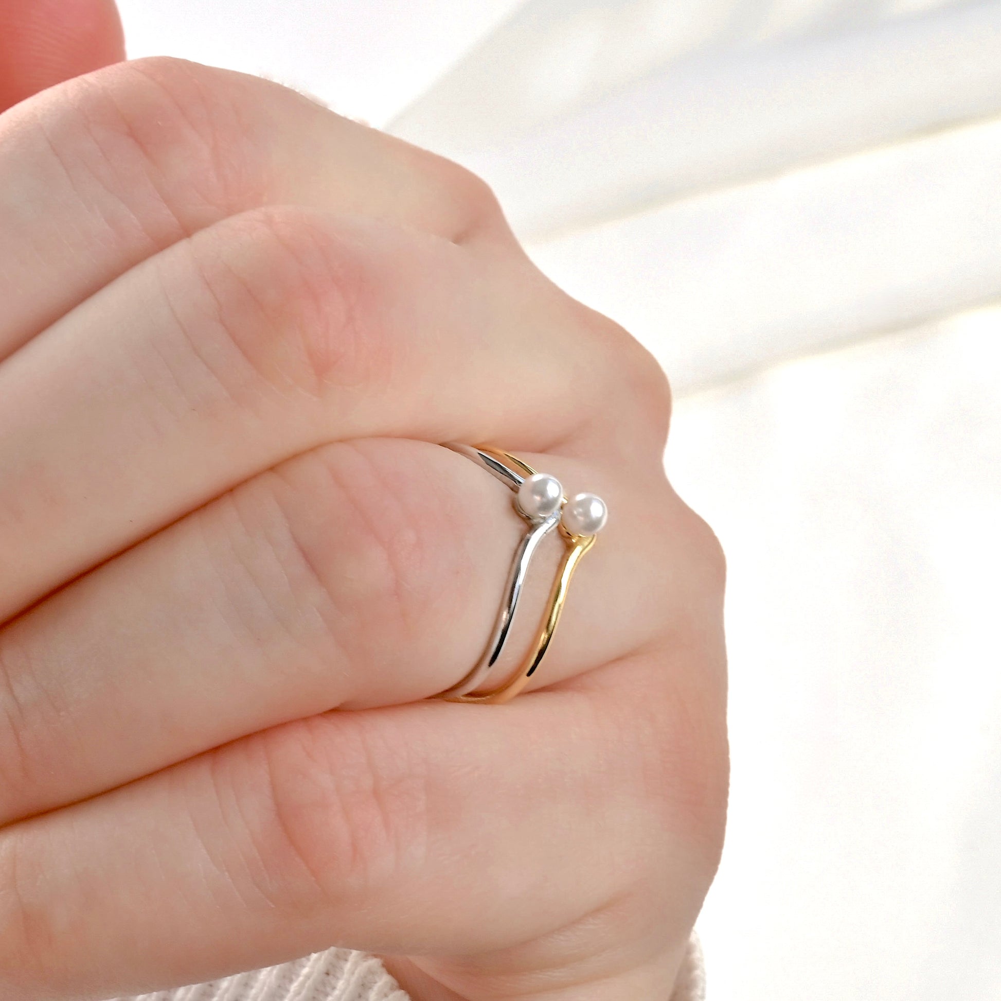 Gold and silver pearl wishbone rings stacked on a finger against a neutral background