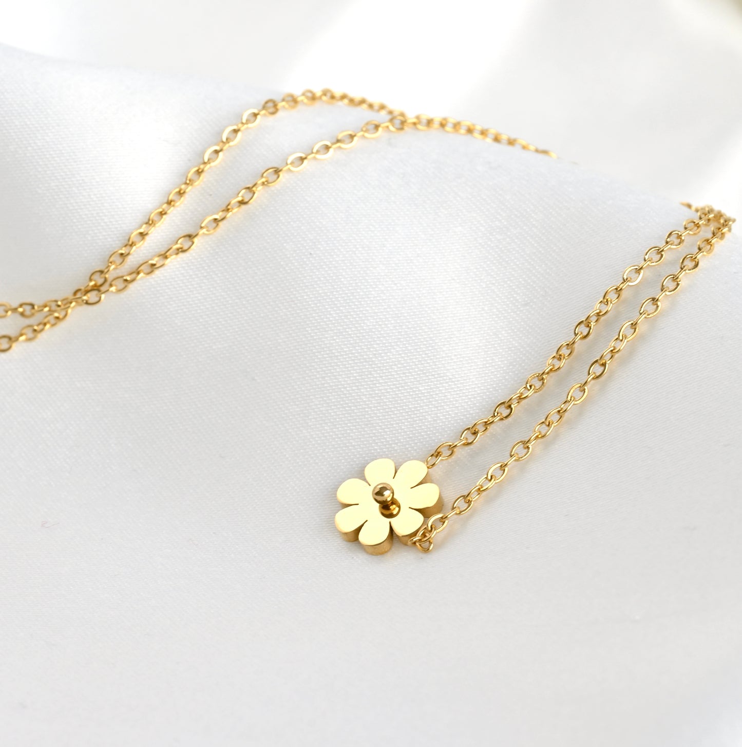 Gold necklace with a flower pendant on a white background showcasing the delicate light gold-toned cable chain the flower charm is attached to.