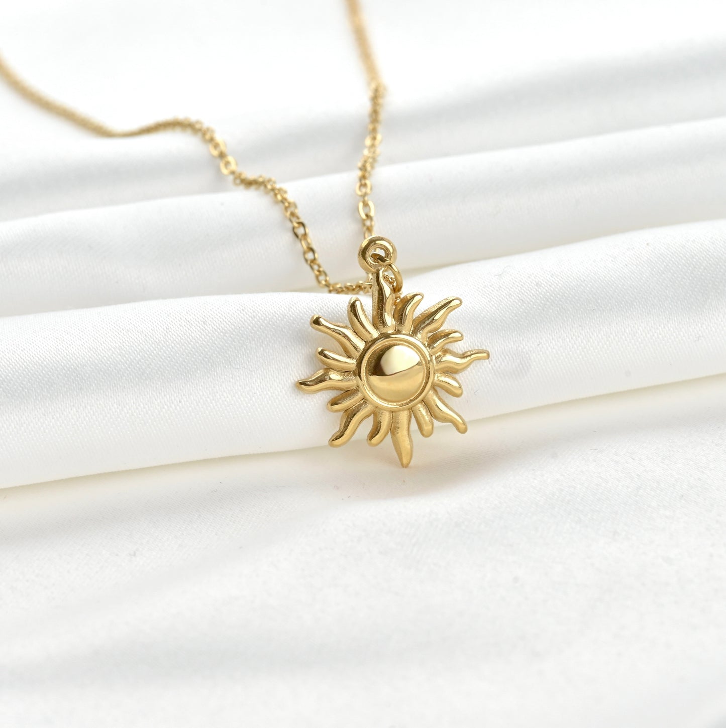 Close up view of gold sun-shaped pendant necklace on a white fabric background