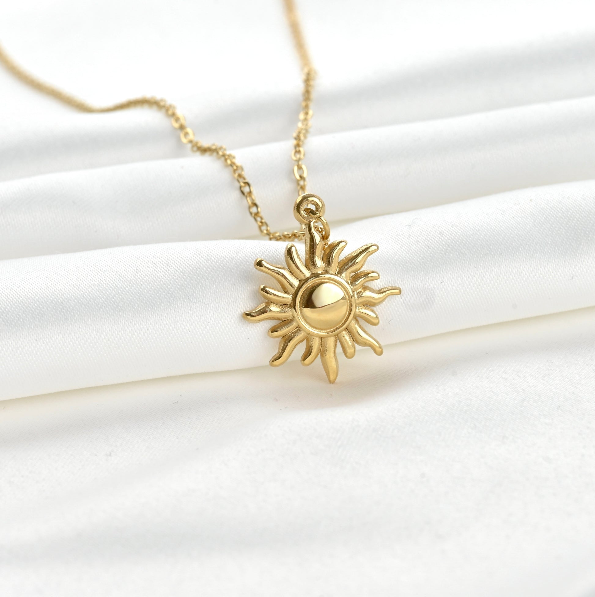 Close up view of gold sun-shaped pendant necklace on a white fabric background