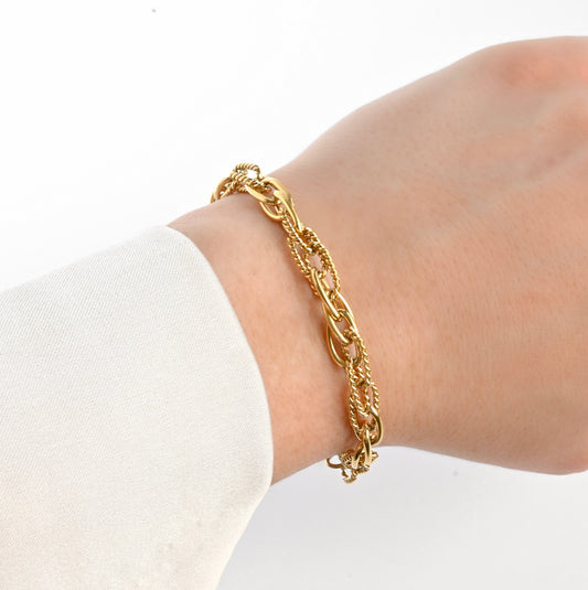 Gold chain bracelet with layered oval links on a wrist with a white background