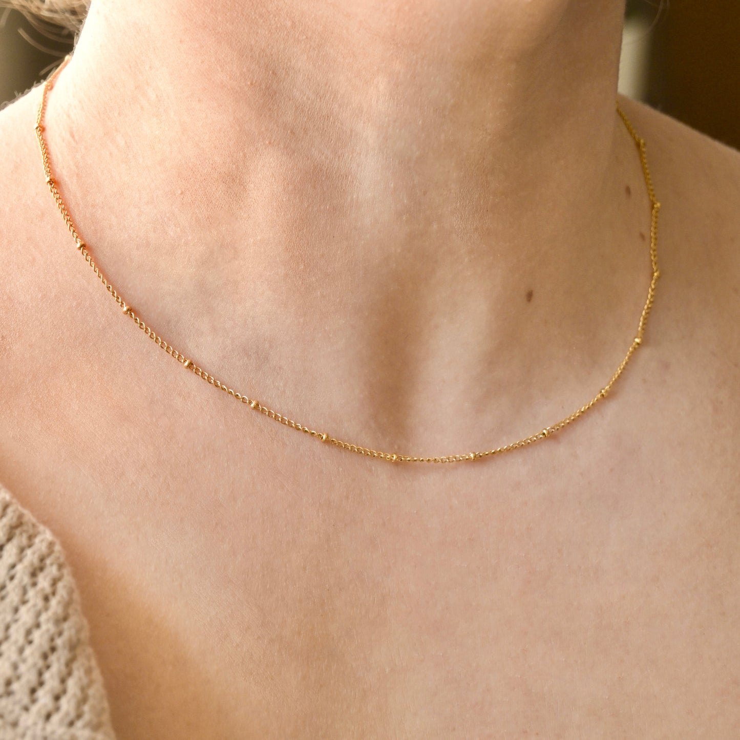Gold beaded chain necklace on a person's neck with a blurred background