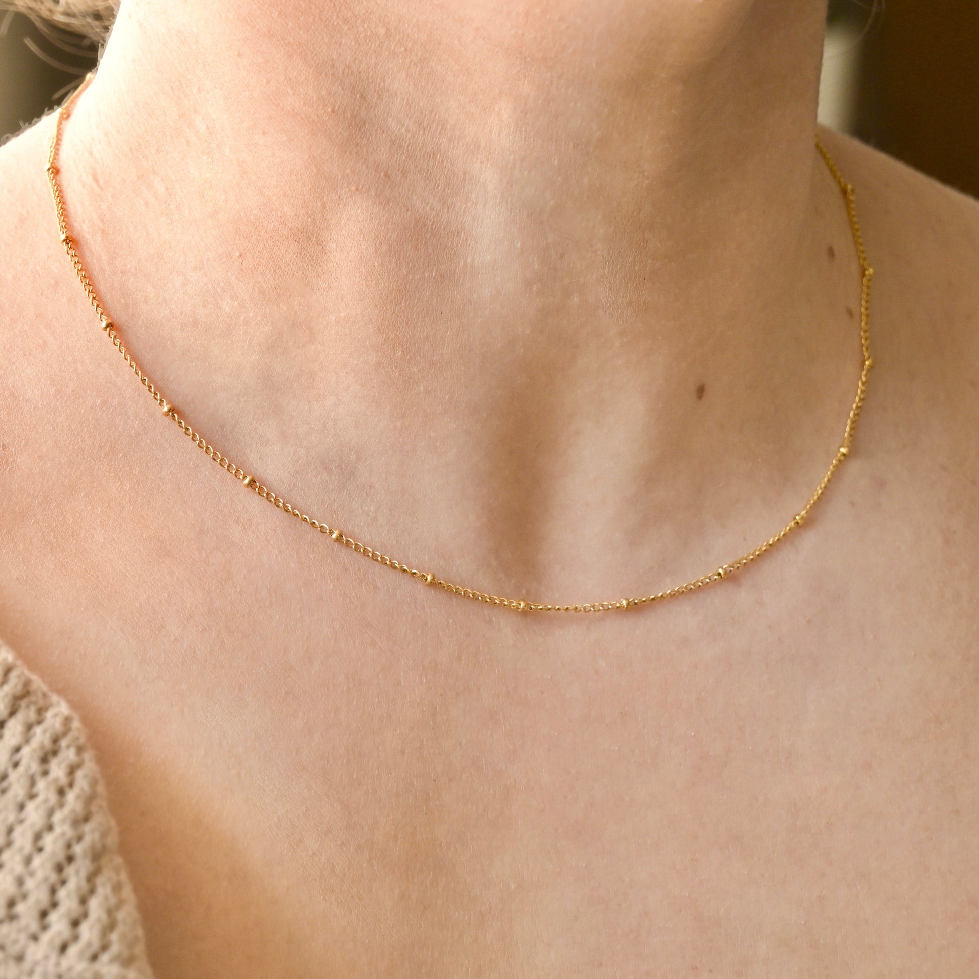 Gold beaded chain necklace on a person's neck with a blurred background