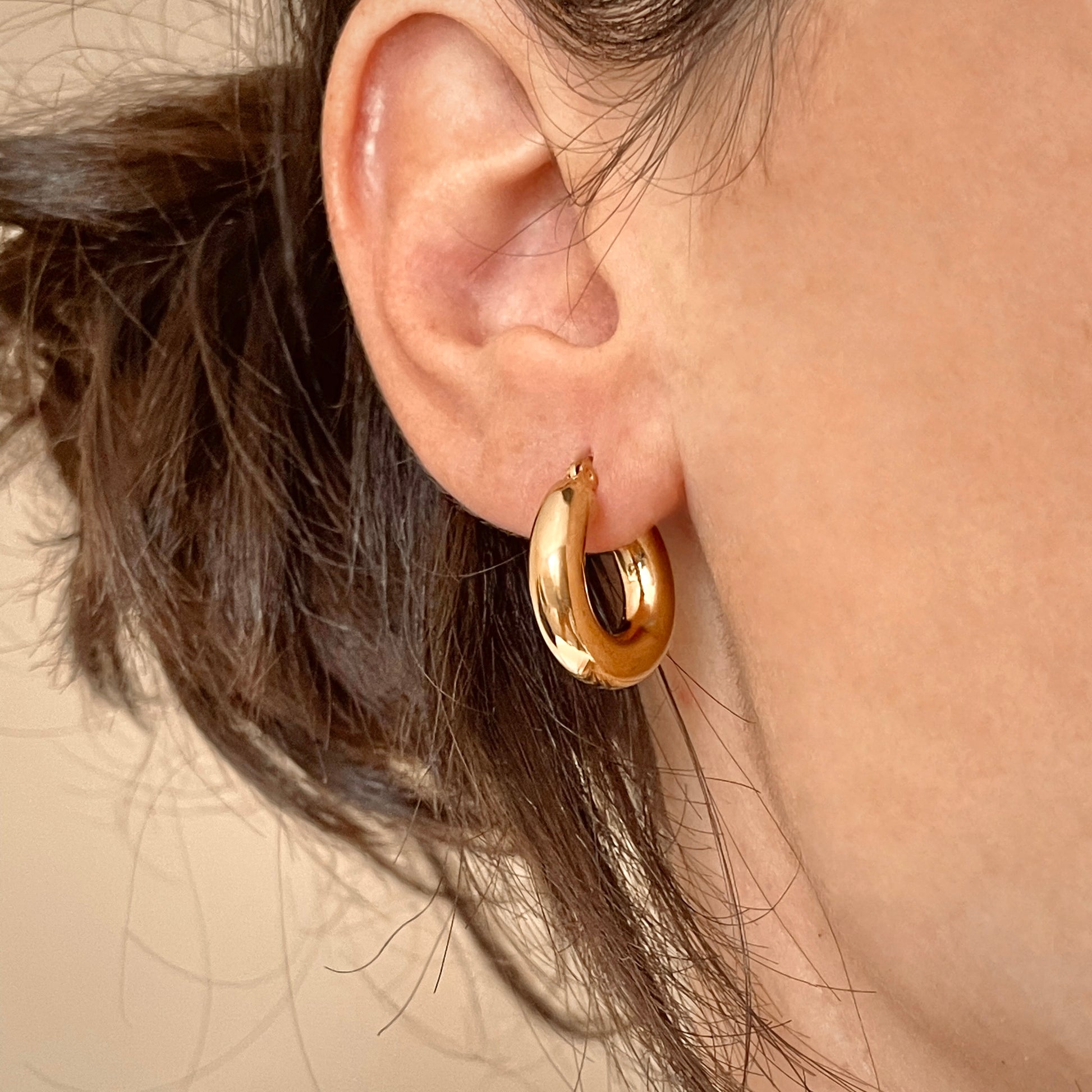 Close-up of a person wearing 20mm  small chunky gold hoop earrings with a neutral background