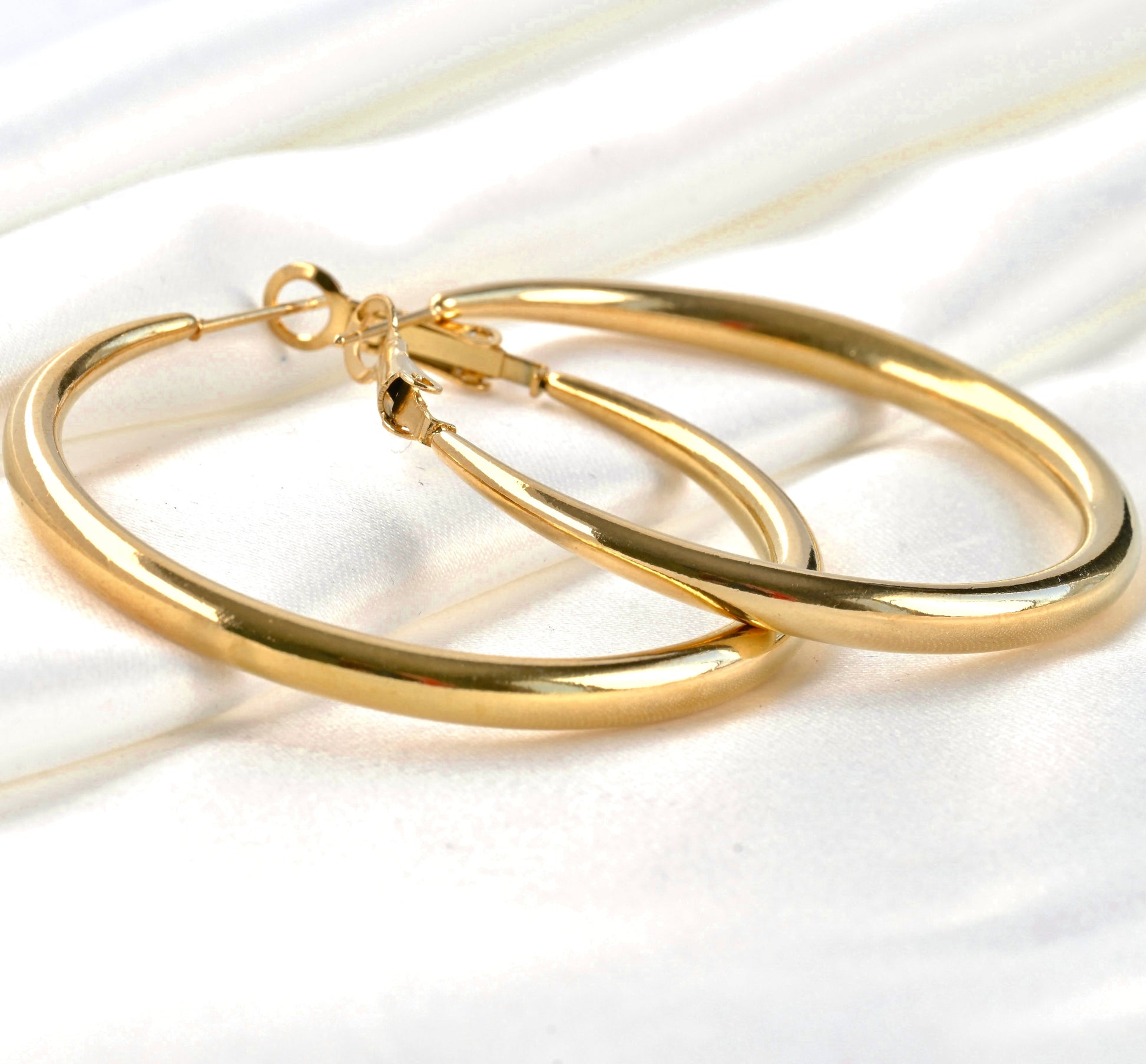 Gold hoop earrings with graduated thickness on a white satin background