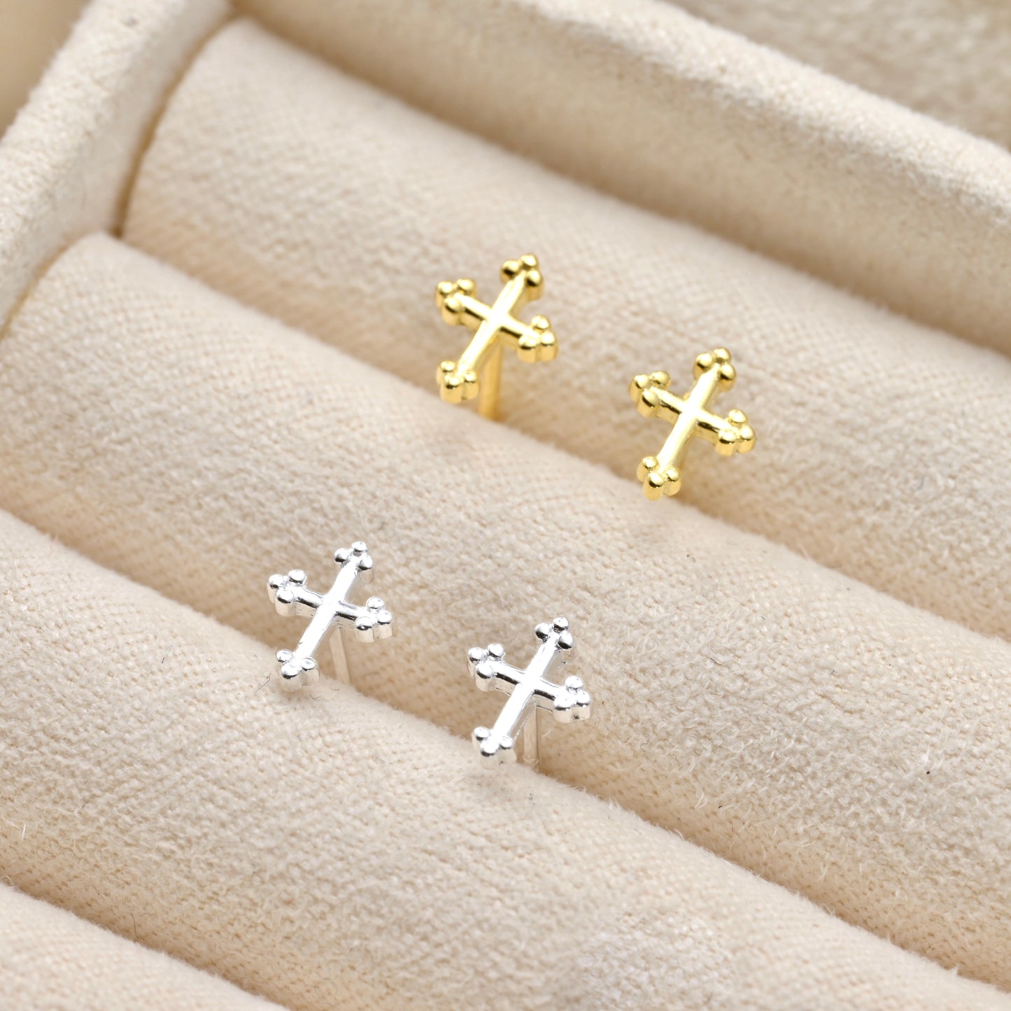 Gold and silver cross-shaped earrings on a soft beige fabric background