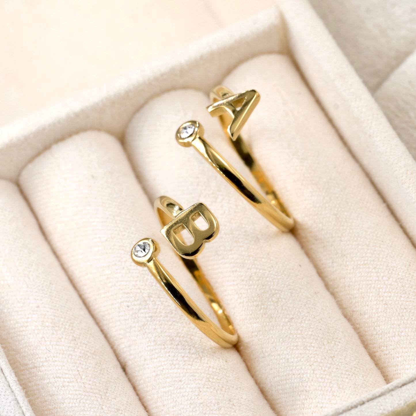 Two gold bezel rings with letter 'A' and 'B' on a beige ring tray