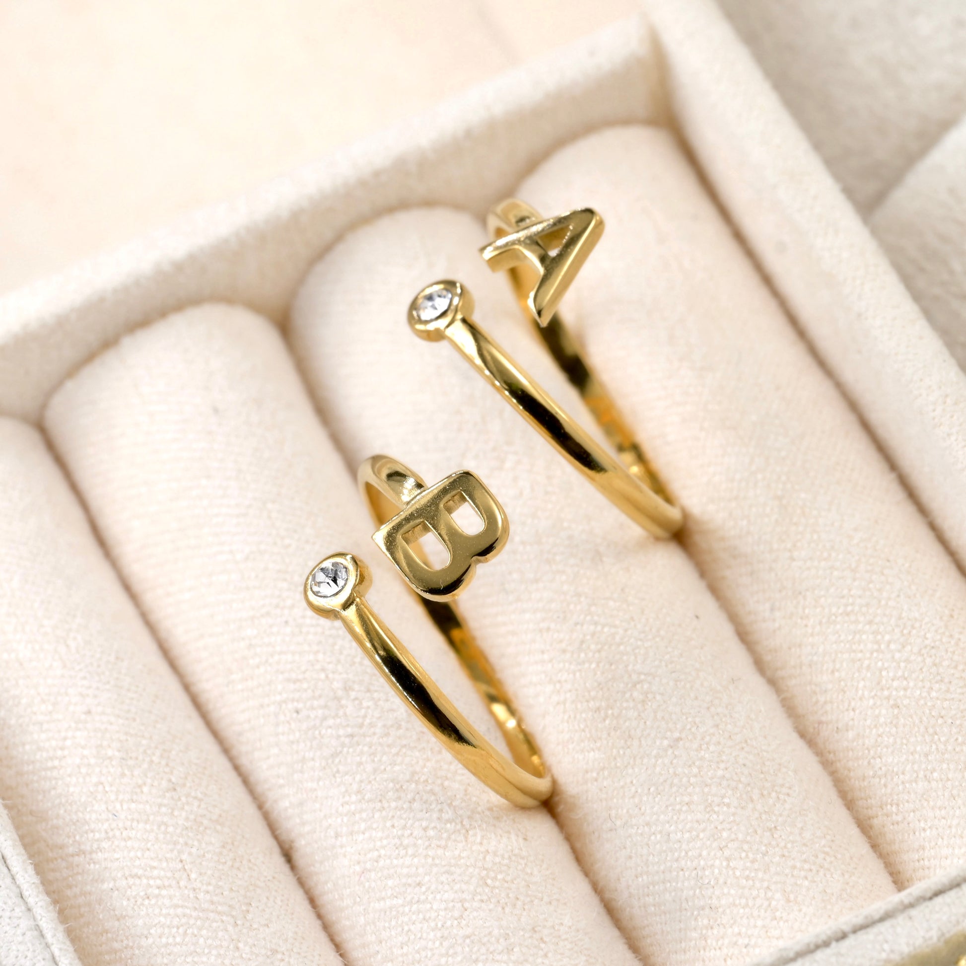Two gold bezel rings with letter 'A' and 'B' on a beige ring tray