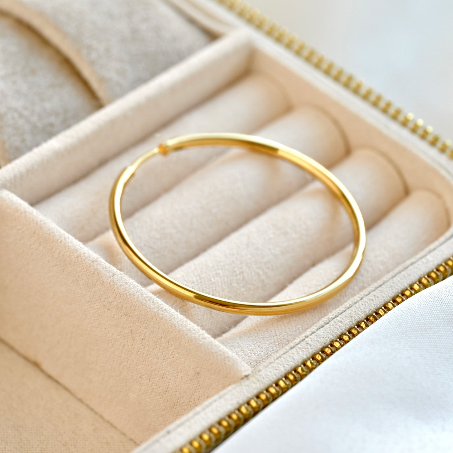 A polished gold infinity hoop earring displayed inside a cream-colored velvet jewelry box.