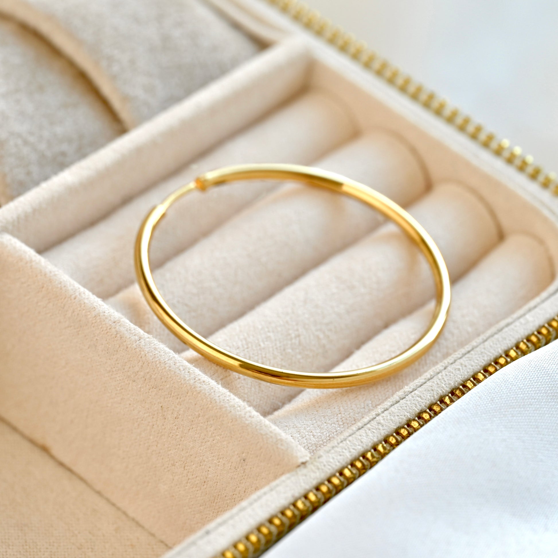 A polished gold infinity hoop earring displayed inside a cream-colored velvet jewelry box.