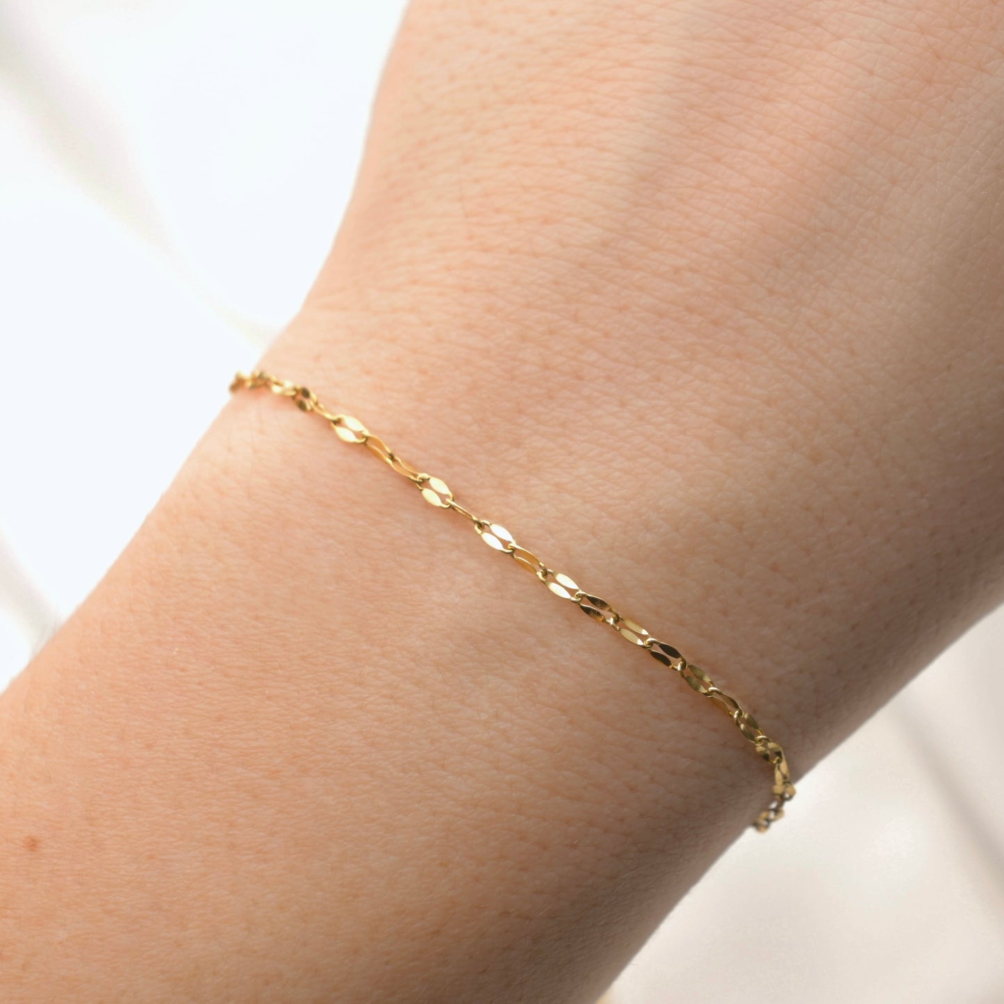 Gold mariner chain bracelet on a wrist with a plain background