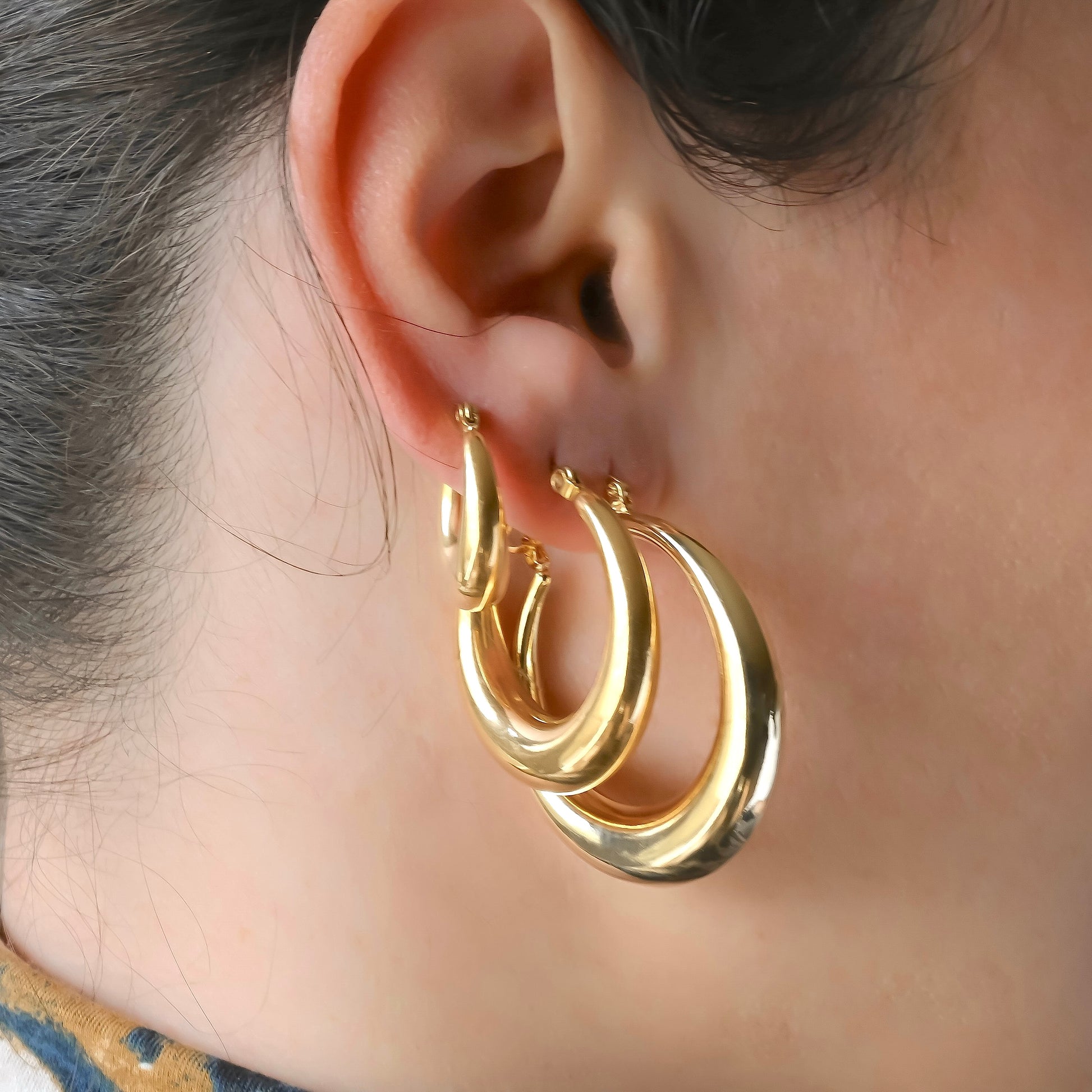 Three gold dome hoop earrings worn by a person with a neutral background