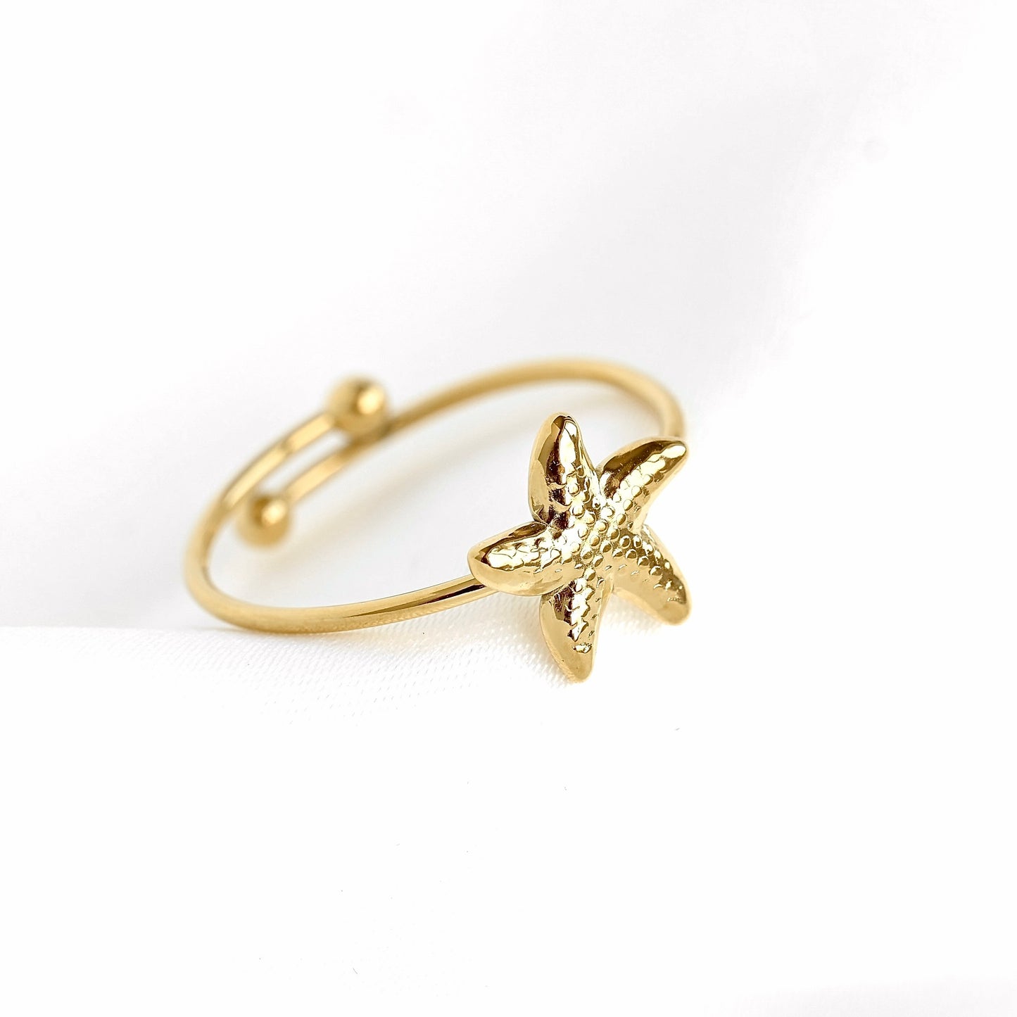 A gold-toned adjustable ring featuring a textured starfish charm, photographed on a clean white background.
