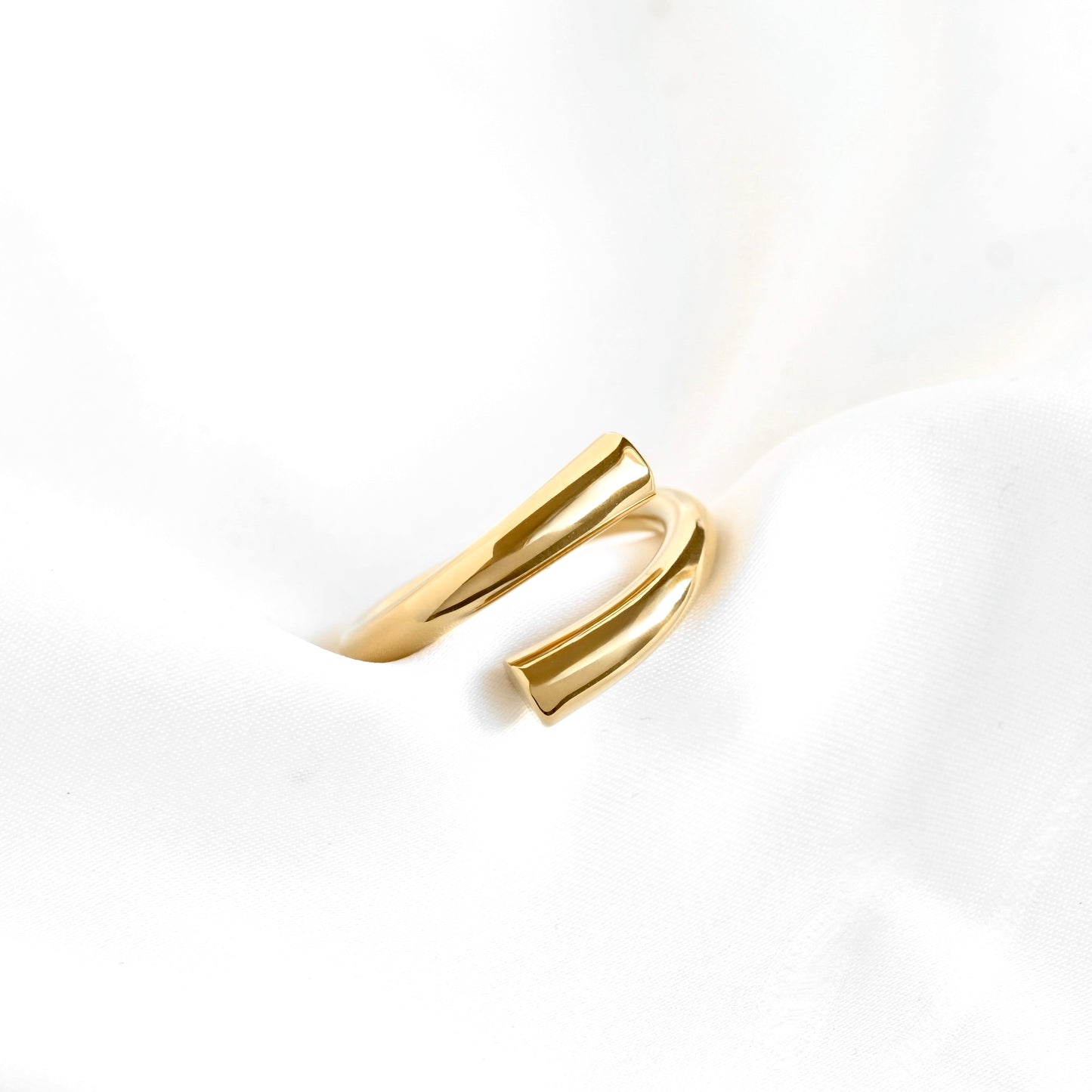 A polished gold open wrap ring displayed on a soft, textured white fabric background.