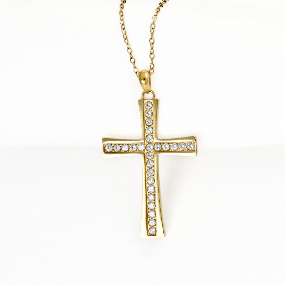 A gold cross pendant necklace adorned with clear pavé stones along the horizontal bar and center intersection, hanging from a delicate gold chain against a plain white background.