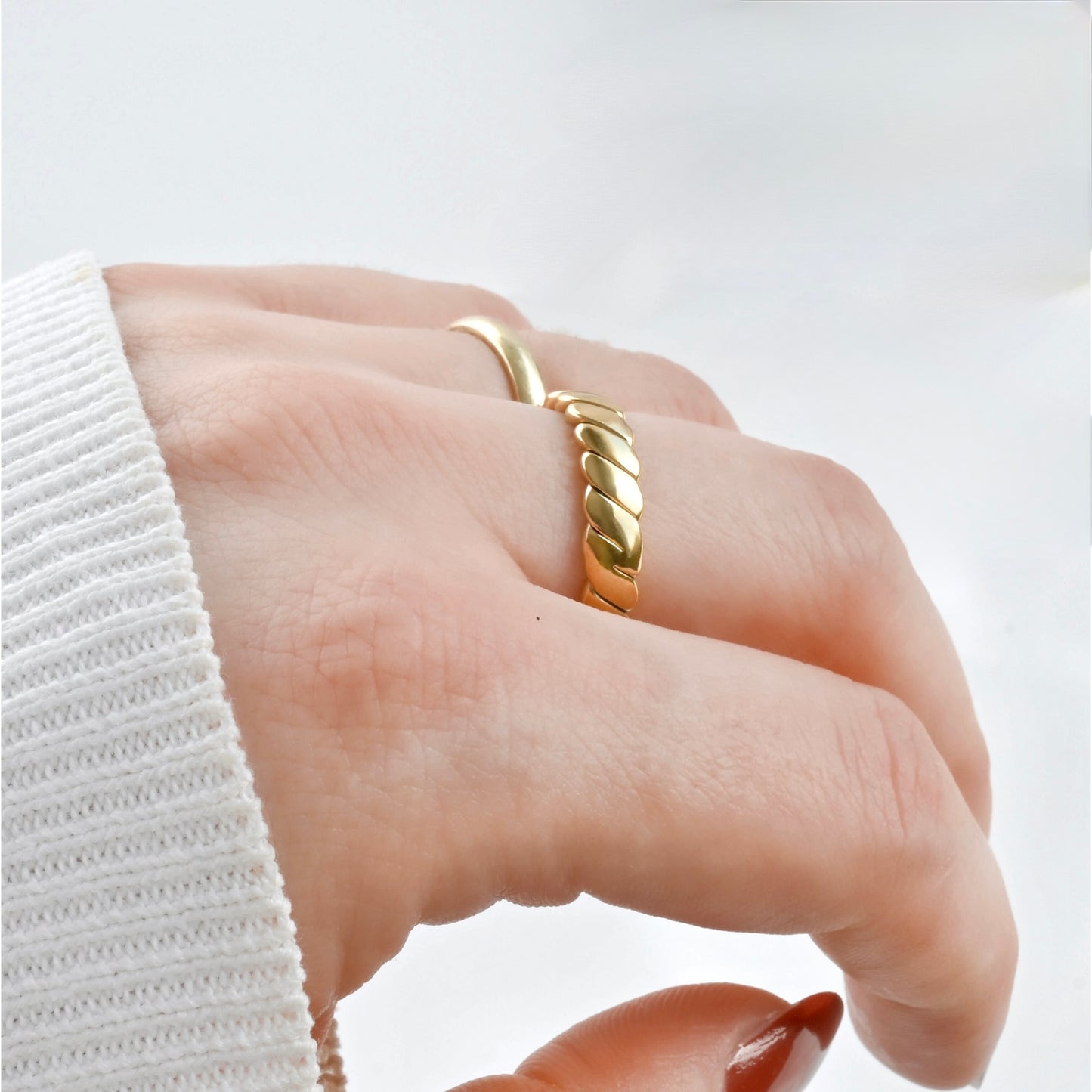 Side view of hand wearing a braided gold ring on a light background