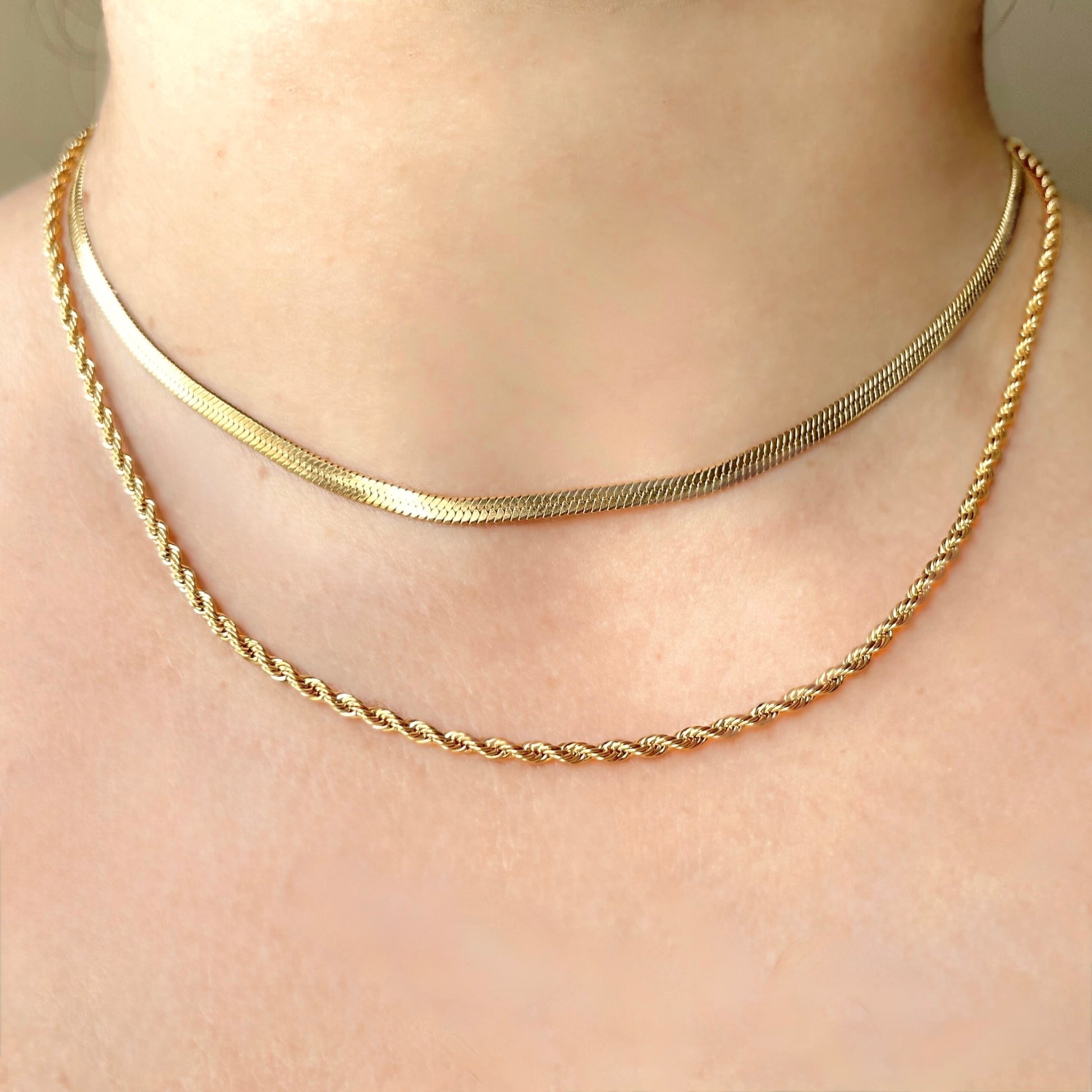 Front view of layered gold necklace set with a herringbone choker and a longer rope chain worn by a person