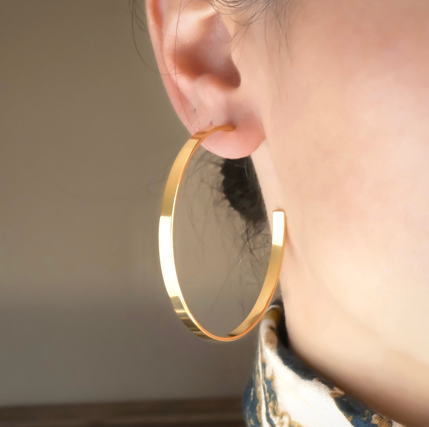 Front view of flat gold C hoop earrings worn by a person with a neutral background