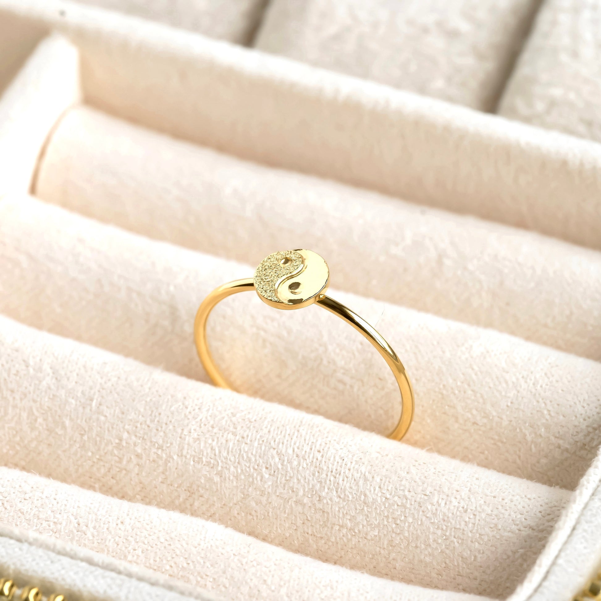 Gold ring with a round design on a beige jewelry box