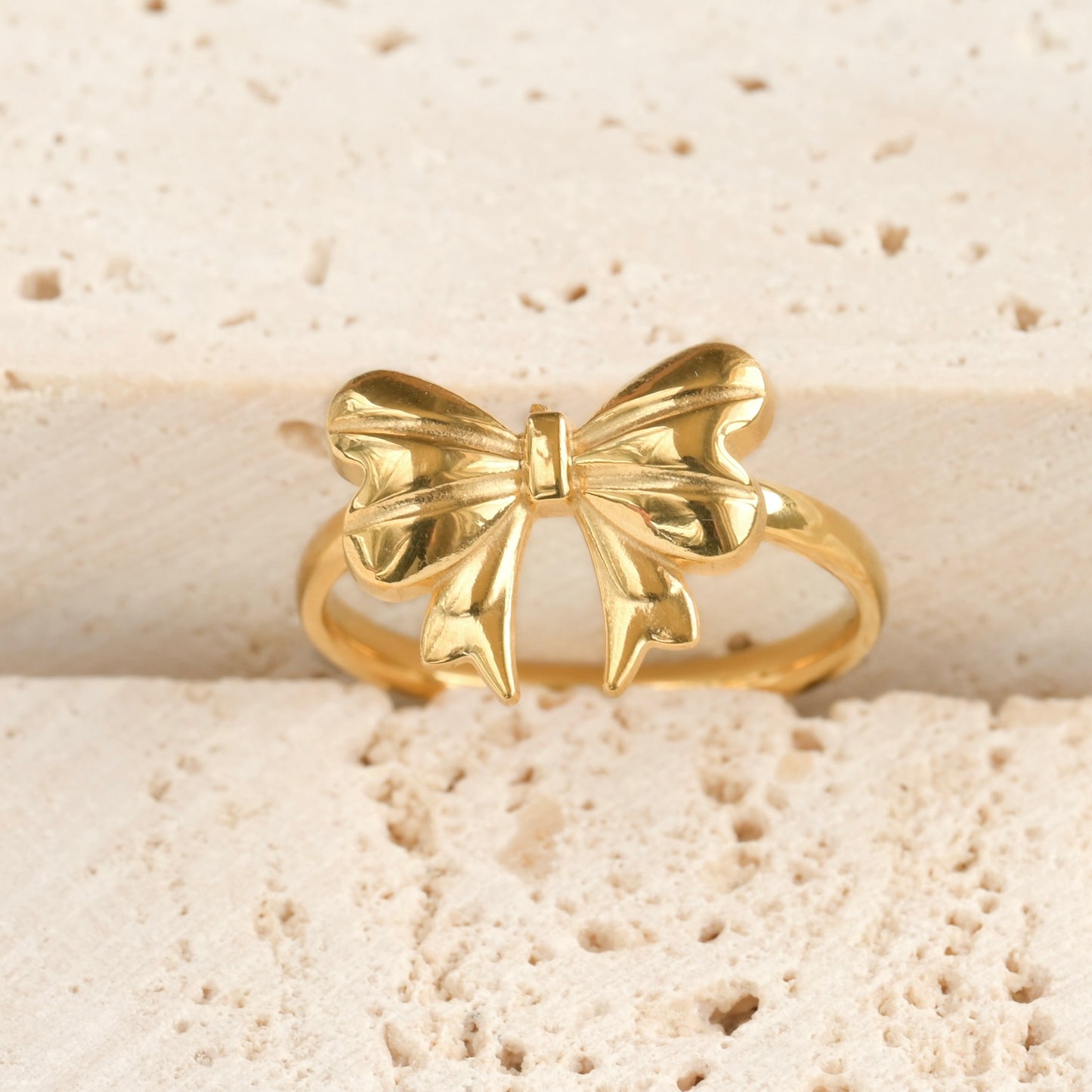 Front view of a gold bow-shaped ring on a textured stone surface