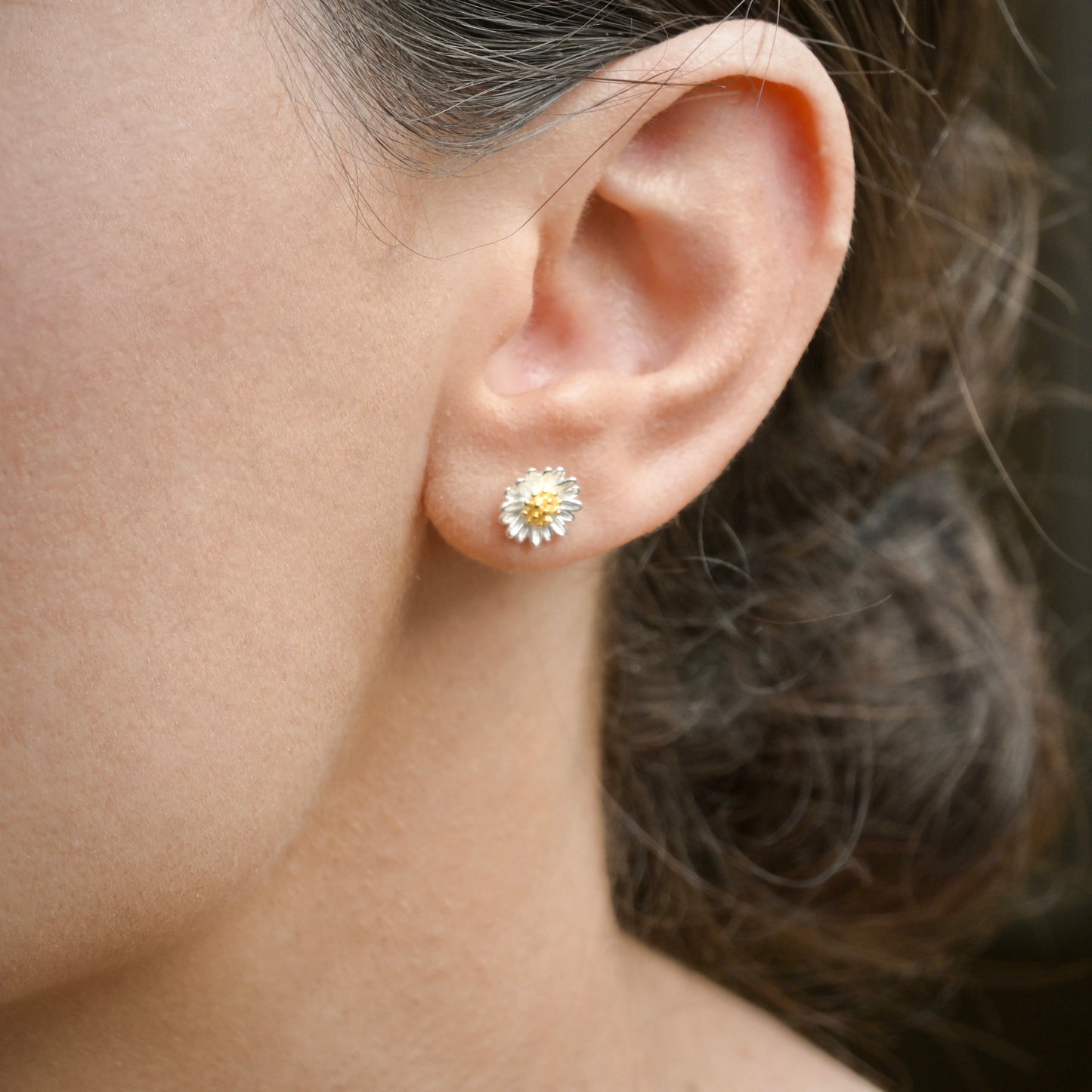 Close-up of an ear wearing small daisy studs with a blurred background
