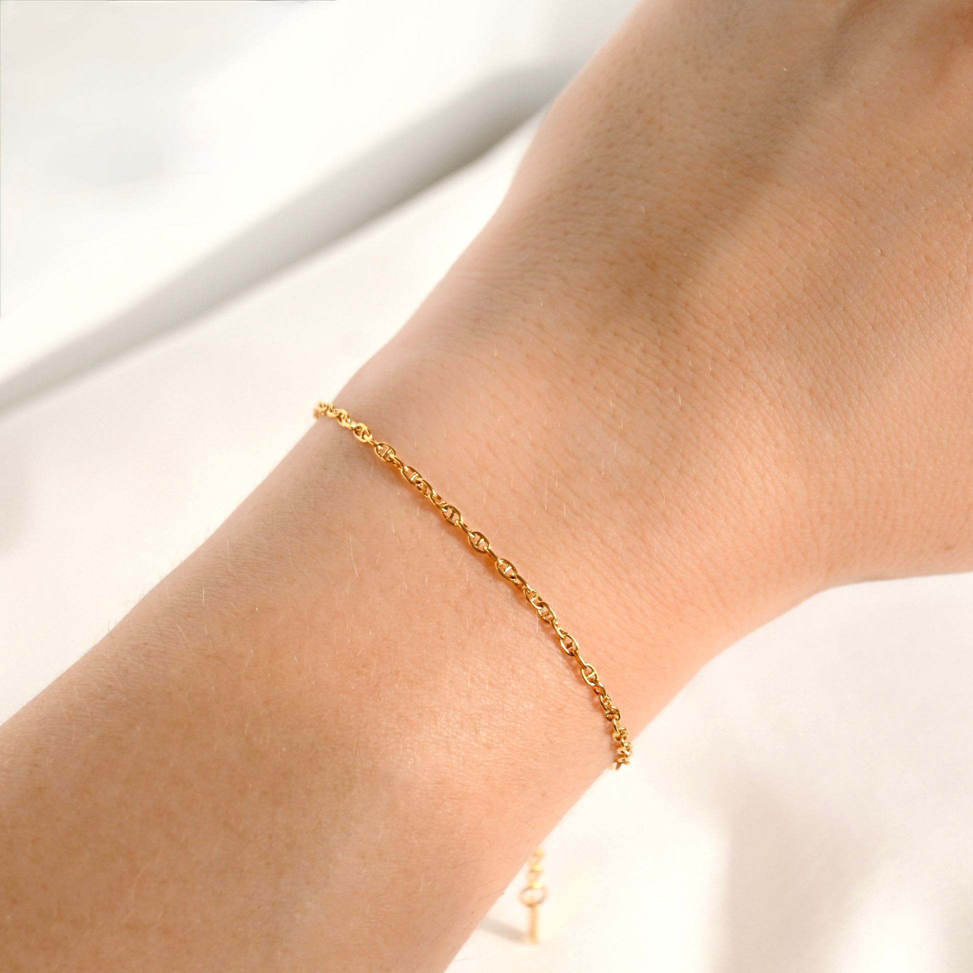 A delicate gold chain bracelet worn on a person's wrist, shown in a close-up shot against a soft, light background.