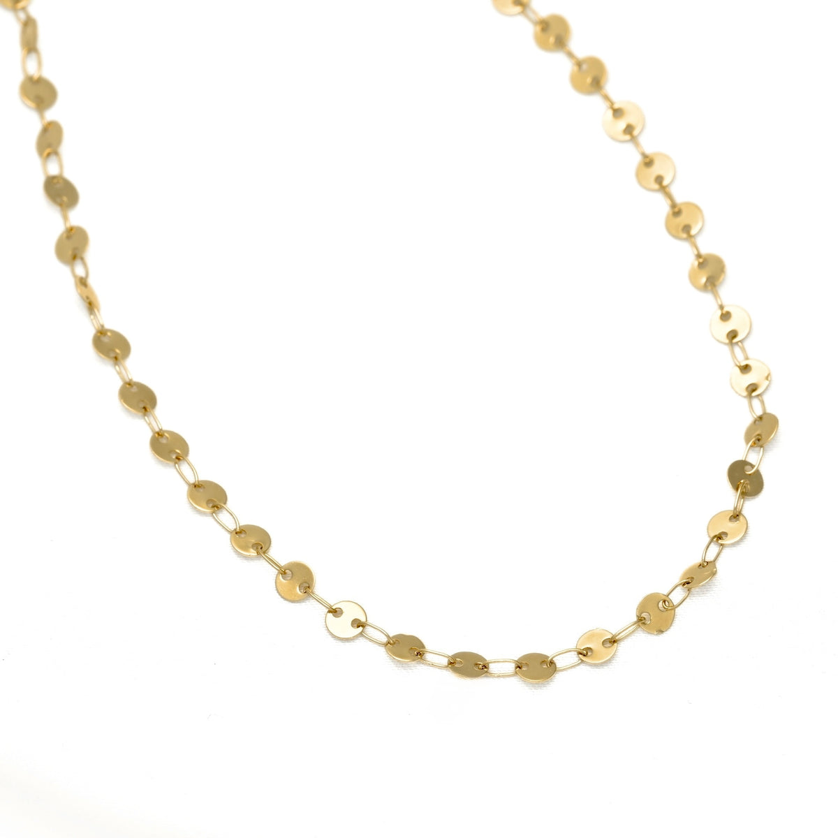 A gold disc-link chain necklace arranged in a gentle curve on a plain white background.