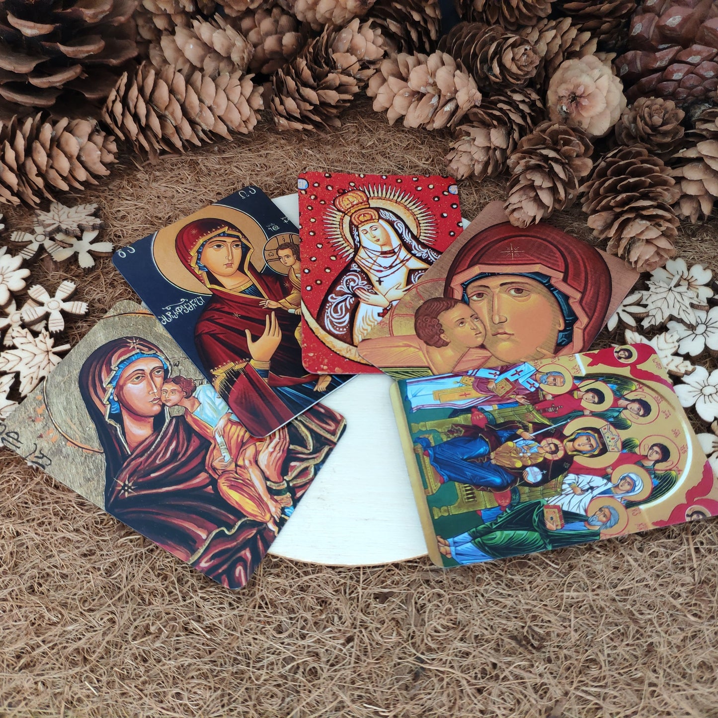 Set of religious-themed cards with magnet on a textured surface with pinecones and flowers.