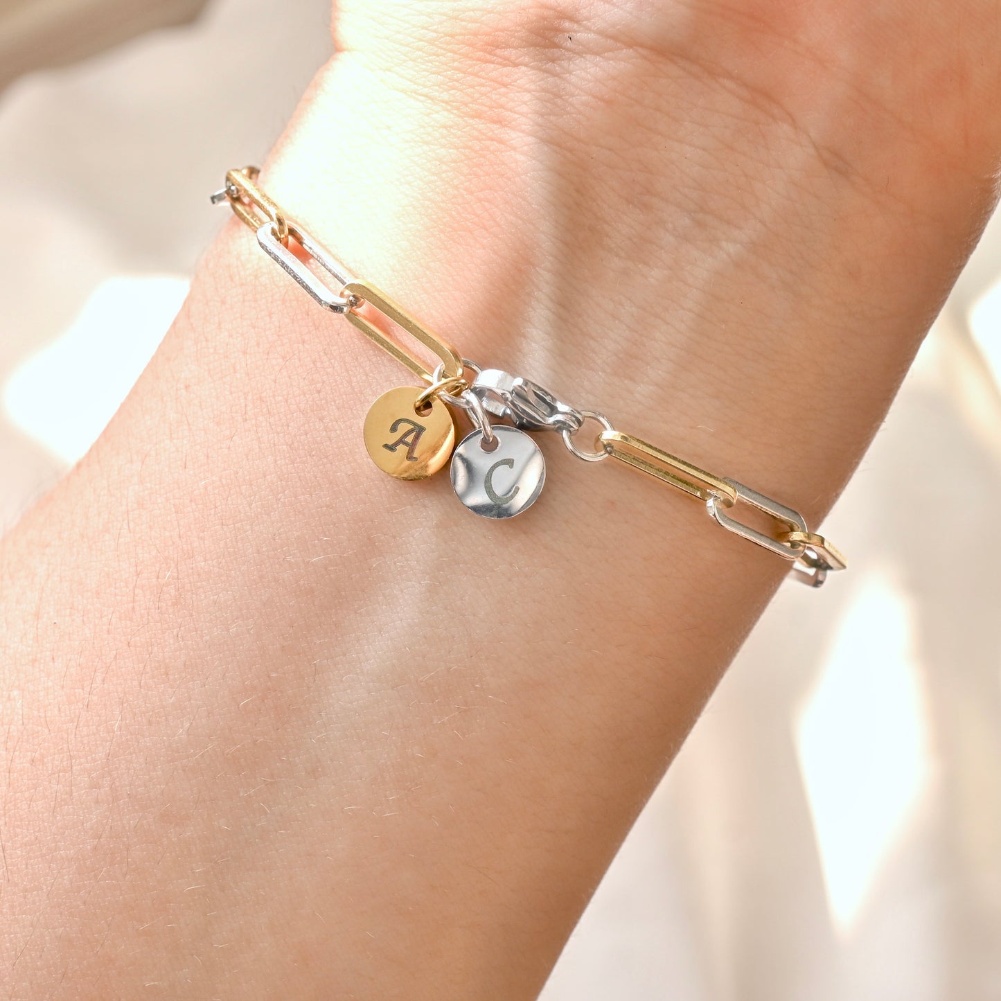 Gold and silver link bracelet with  gold and silver engraved charms at the clasp on a wrist against a neutral background