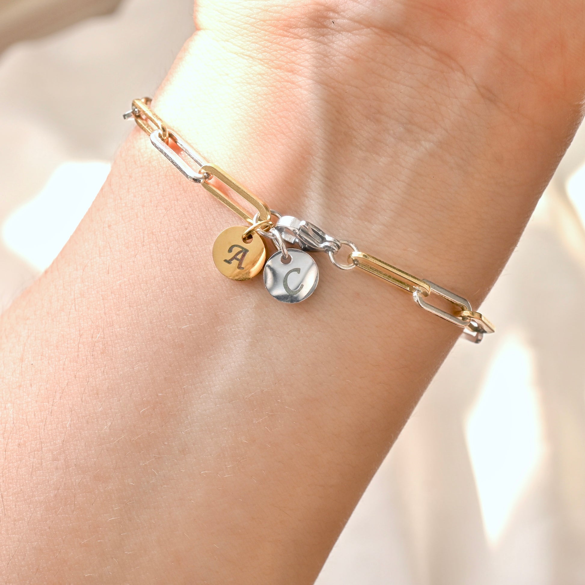 Gold and silver link bracelet with  gold and silver engraved charms at the clasp on a wrist against a neutral background