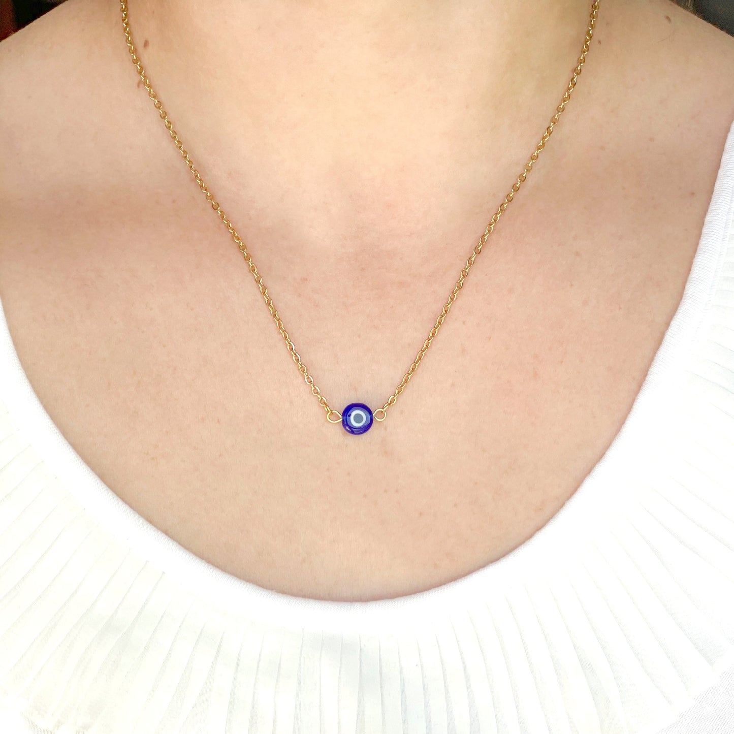 Gold necklace with a blue evil eye pendant on a white shirt