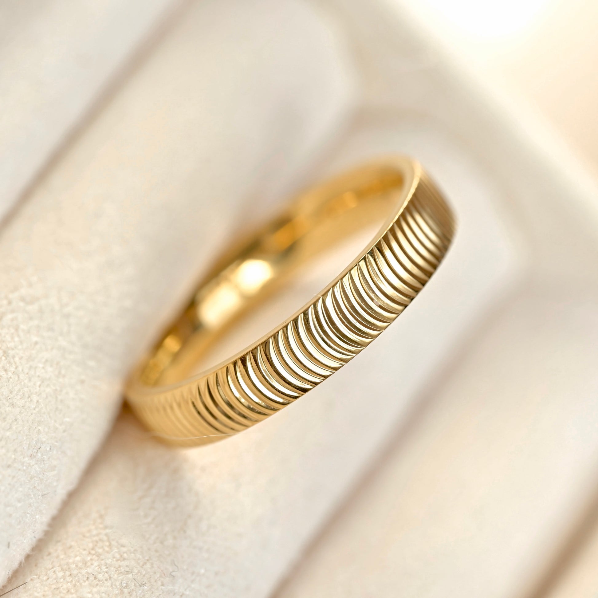 A gold band ring with a textured, ridged exterior, resting on a soft beige velvet jewelry display.