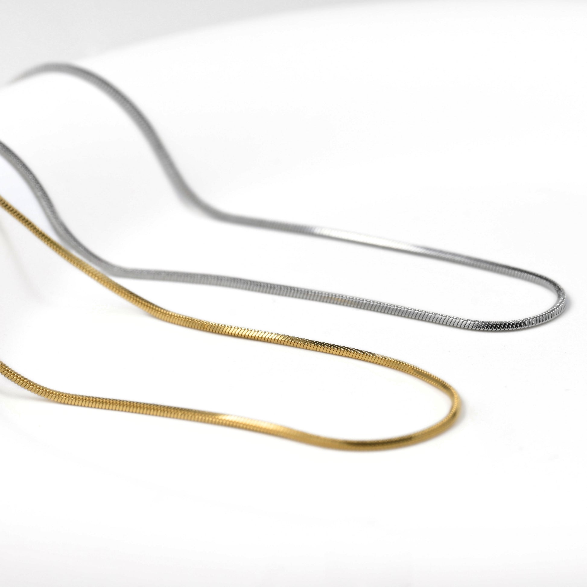 Two metallic chains, one gold and one silver, on a white background.