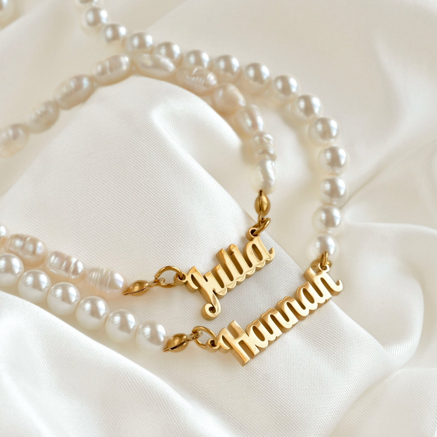 Gold name necklaces with freshwater and shell pearls with a white fabric background