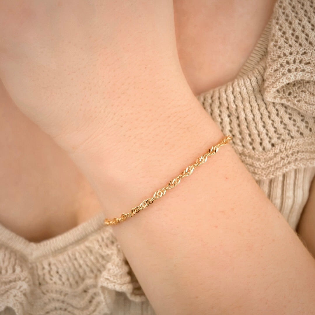 Dainty gold twisted bracelet on a person's wrist with a neutral background