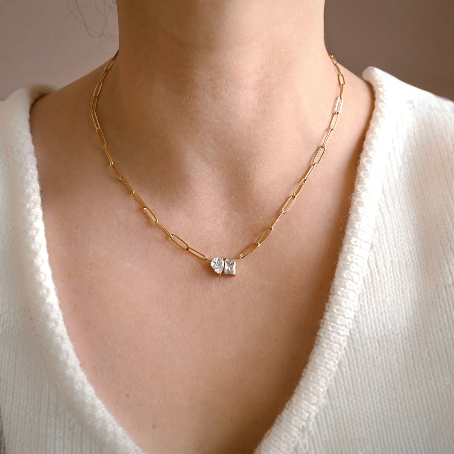 Gold chain necklace with a diamond pendant worn by a person in a white sweater.