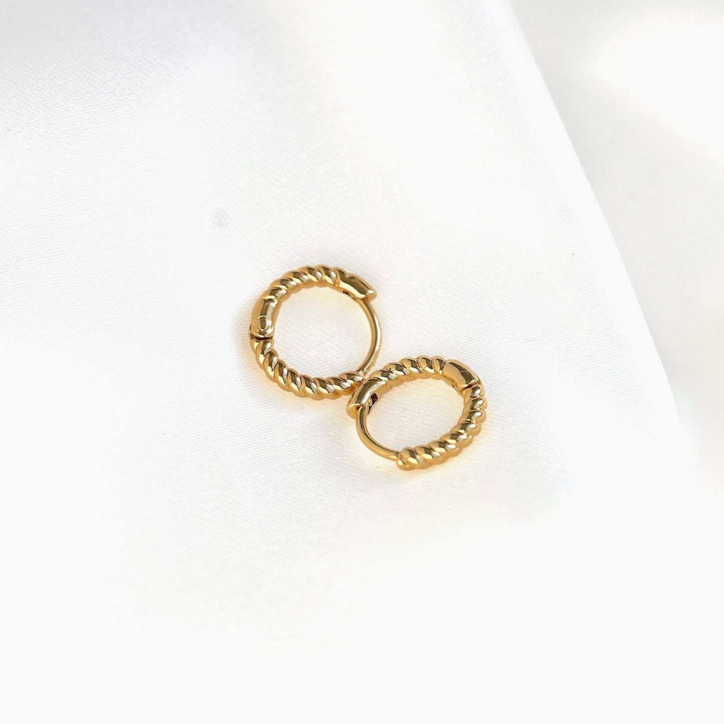 A pair of small gold huggie hoop earrings with a twisted rope texture, displayed on a clean white background.