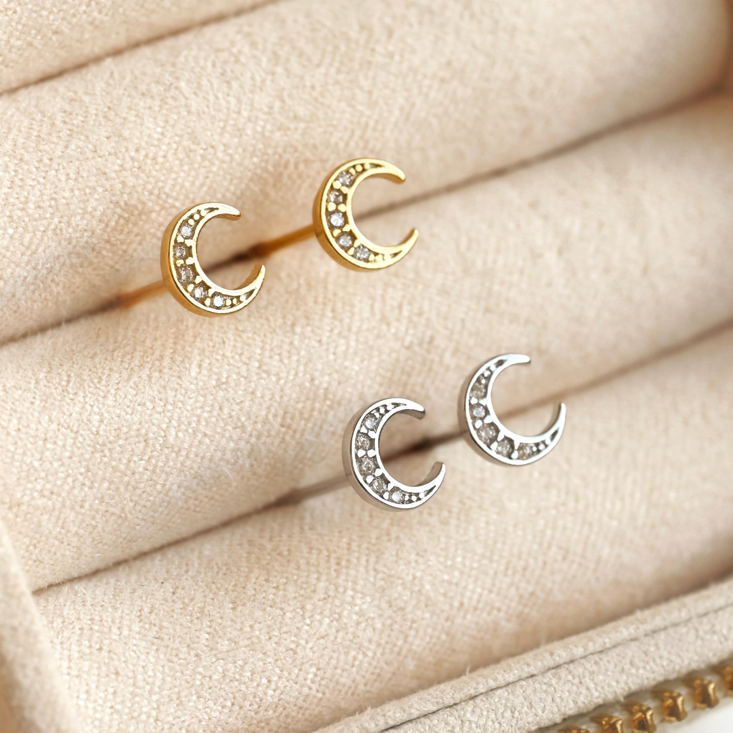 Pair of gold and silver crescent moon stud earrings on a beige fabric background
