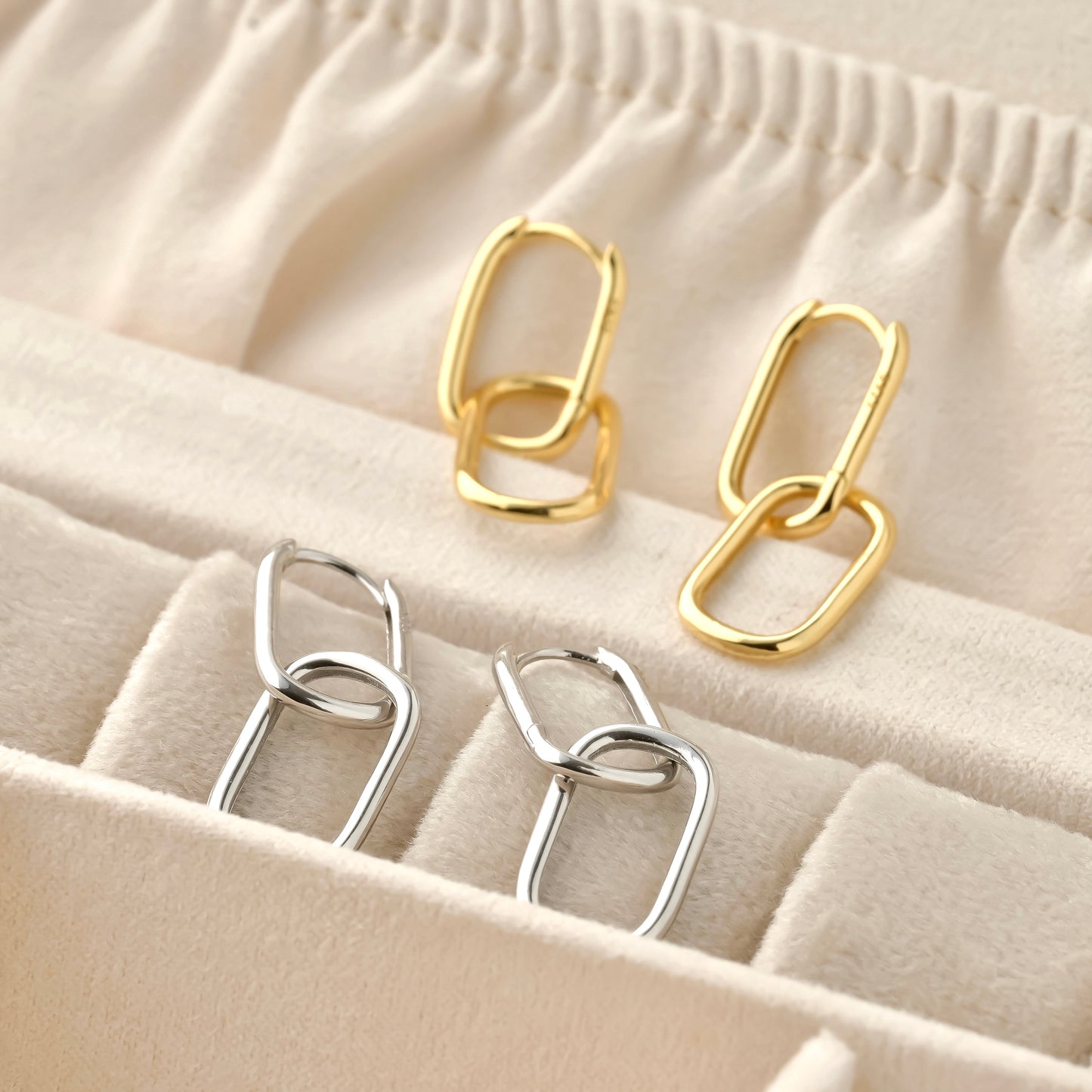 A pair of solid gold and silver chain-style earrings on a beige fabric background
