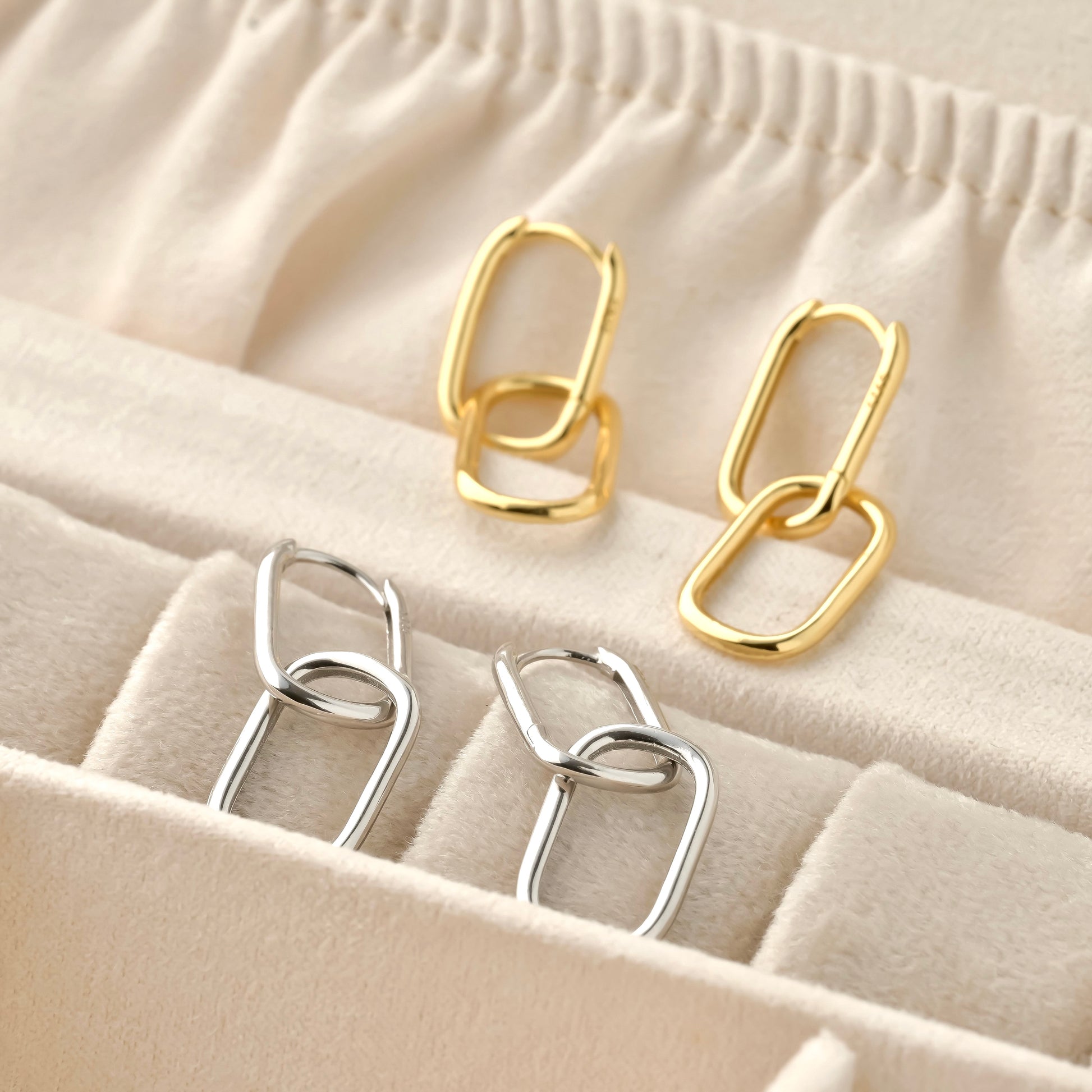 A pair of solid gold and silver chain-style earrings on a beige fabric background