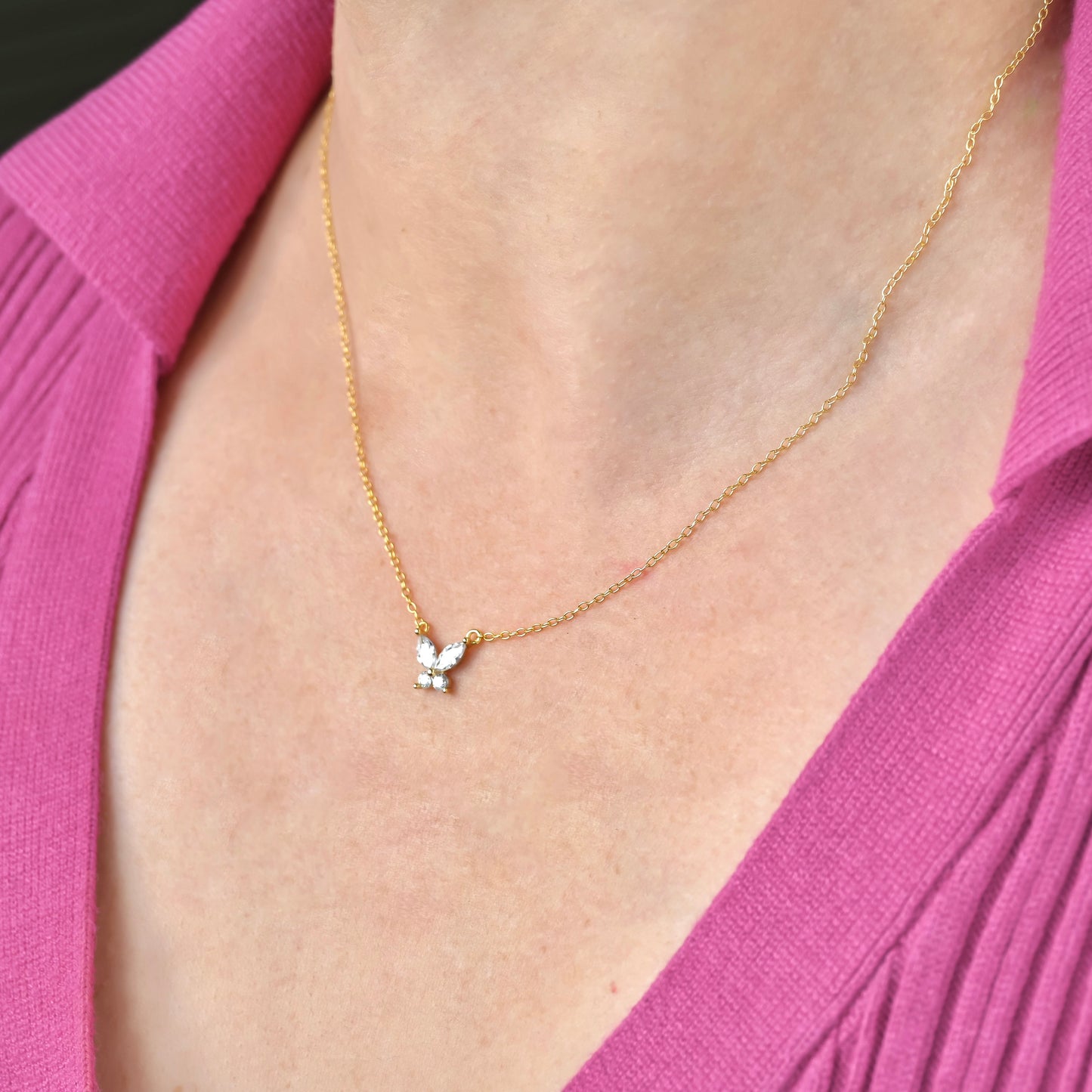 Gold necklace with a small butterfly pendant worn by a person in a pink garment.