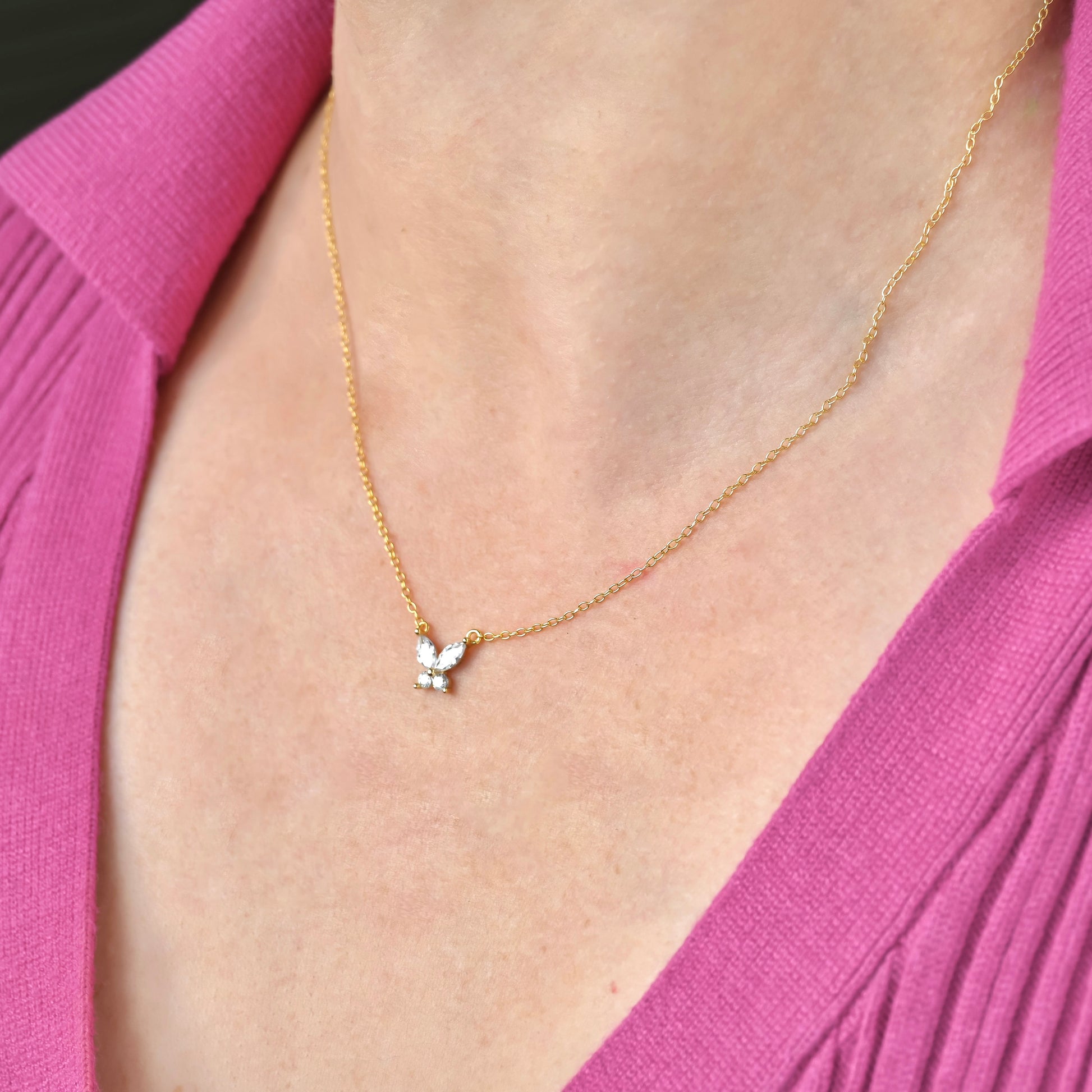 Gold necklace with a small butterfly pendant worn by a person in a pink garment.