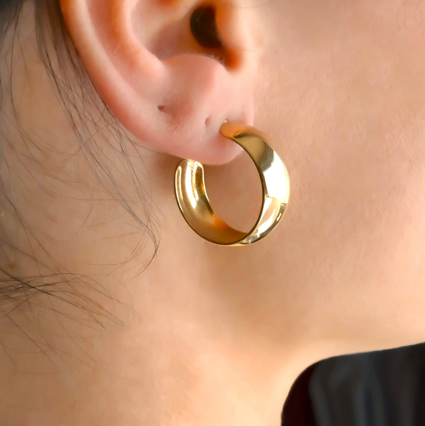 Side view of gold dome earrings worn by a person with a neutral background 