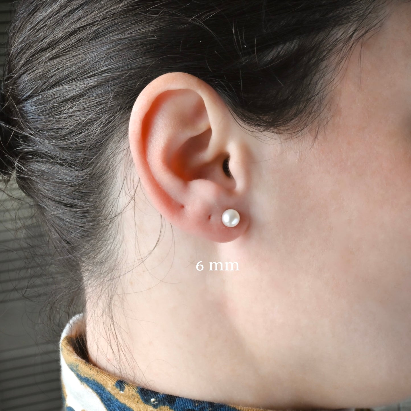 Close-up of an ear wearing a pearl stud earring with '6 mm' label.