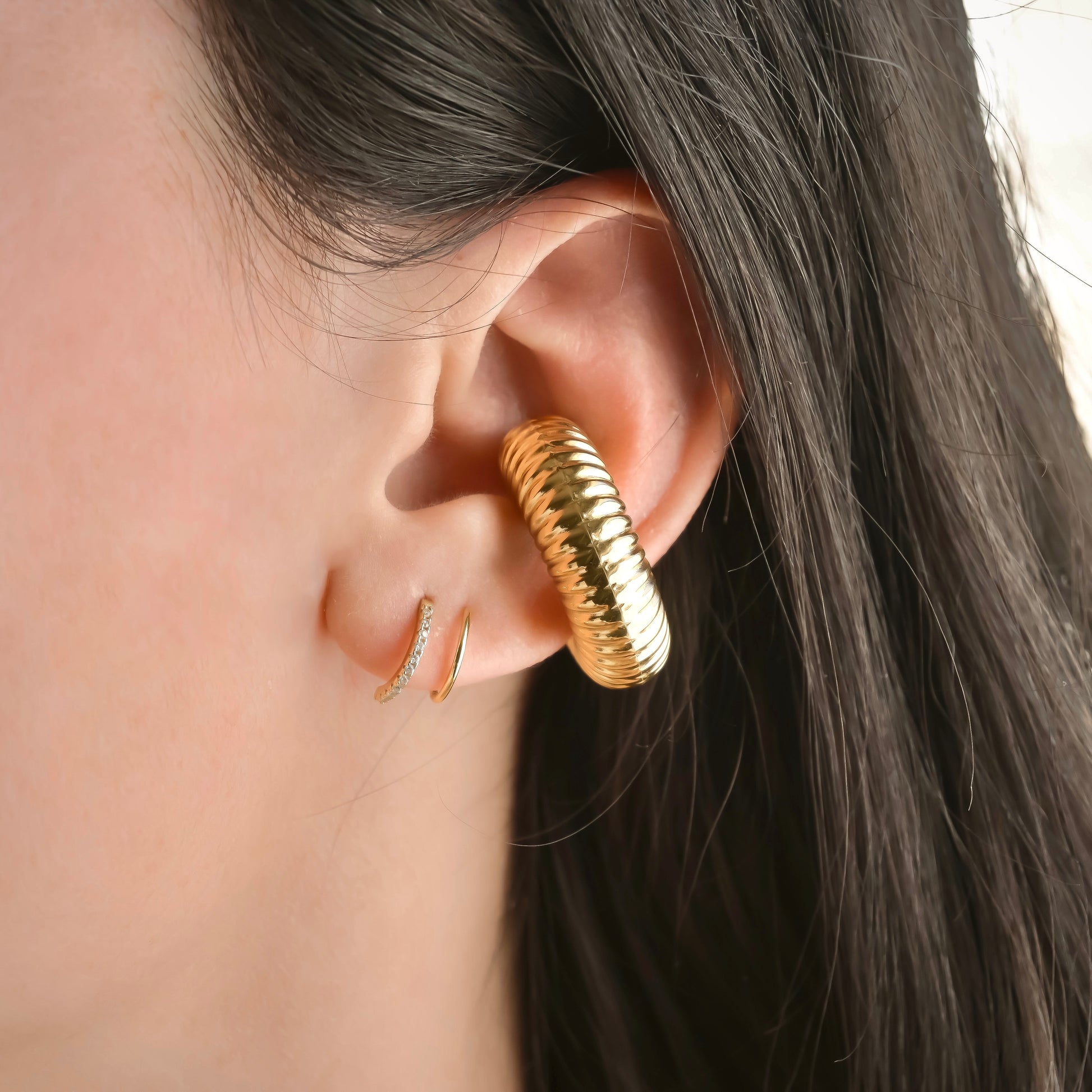 Close-up of an ear wearing textured gold cuff hoops with a blurred background